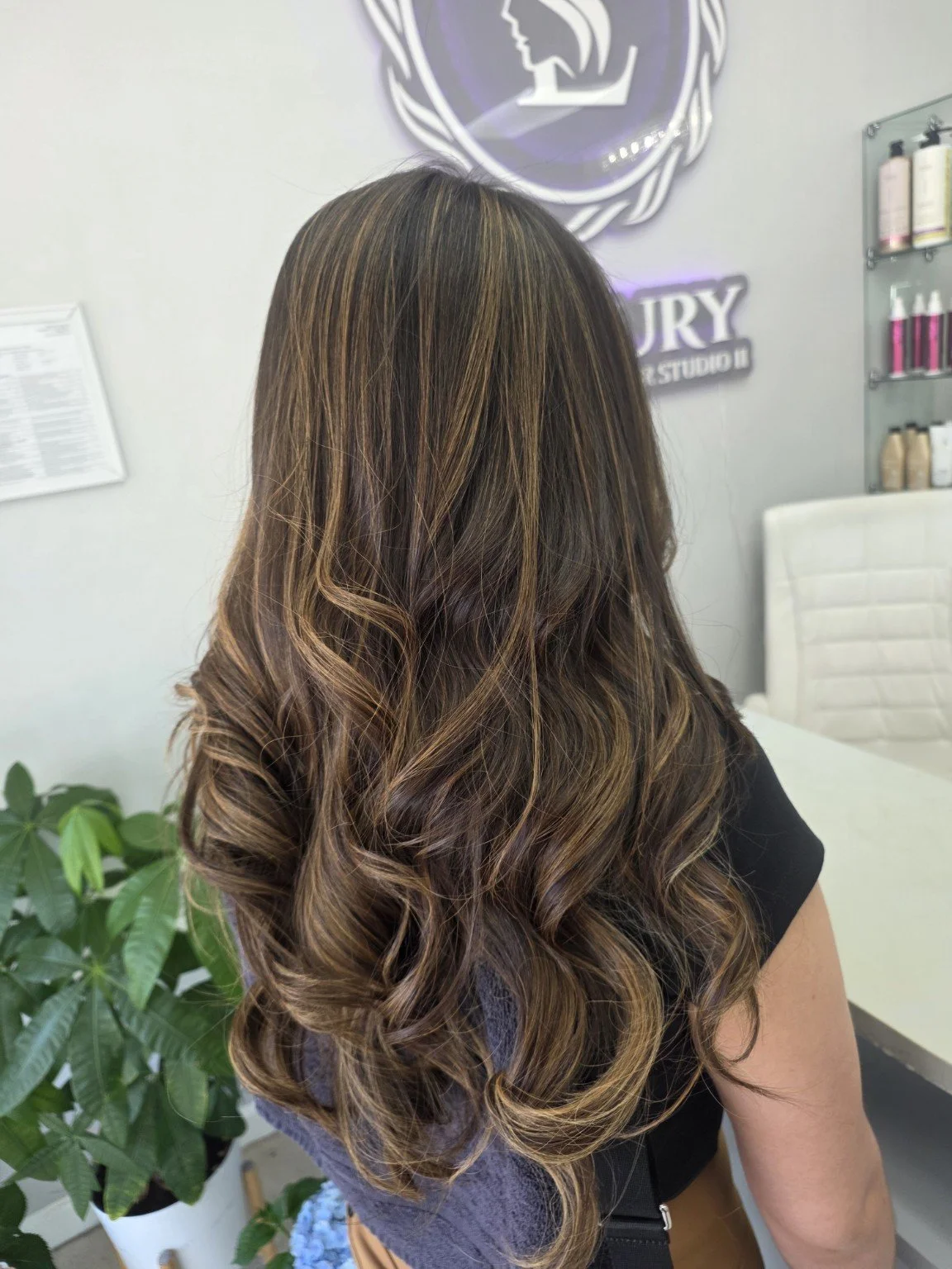 Long brunette hair with soft highlights and curls, styled at Luxury Hair Studio II