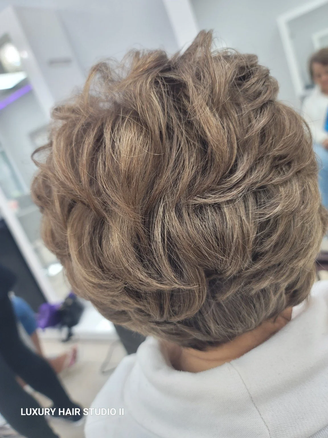 Close-up of a person's head showcasing a styled short, curly, blonde hairdo in a salon setting.