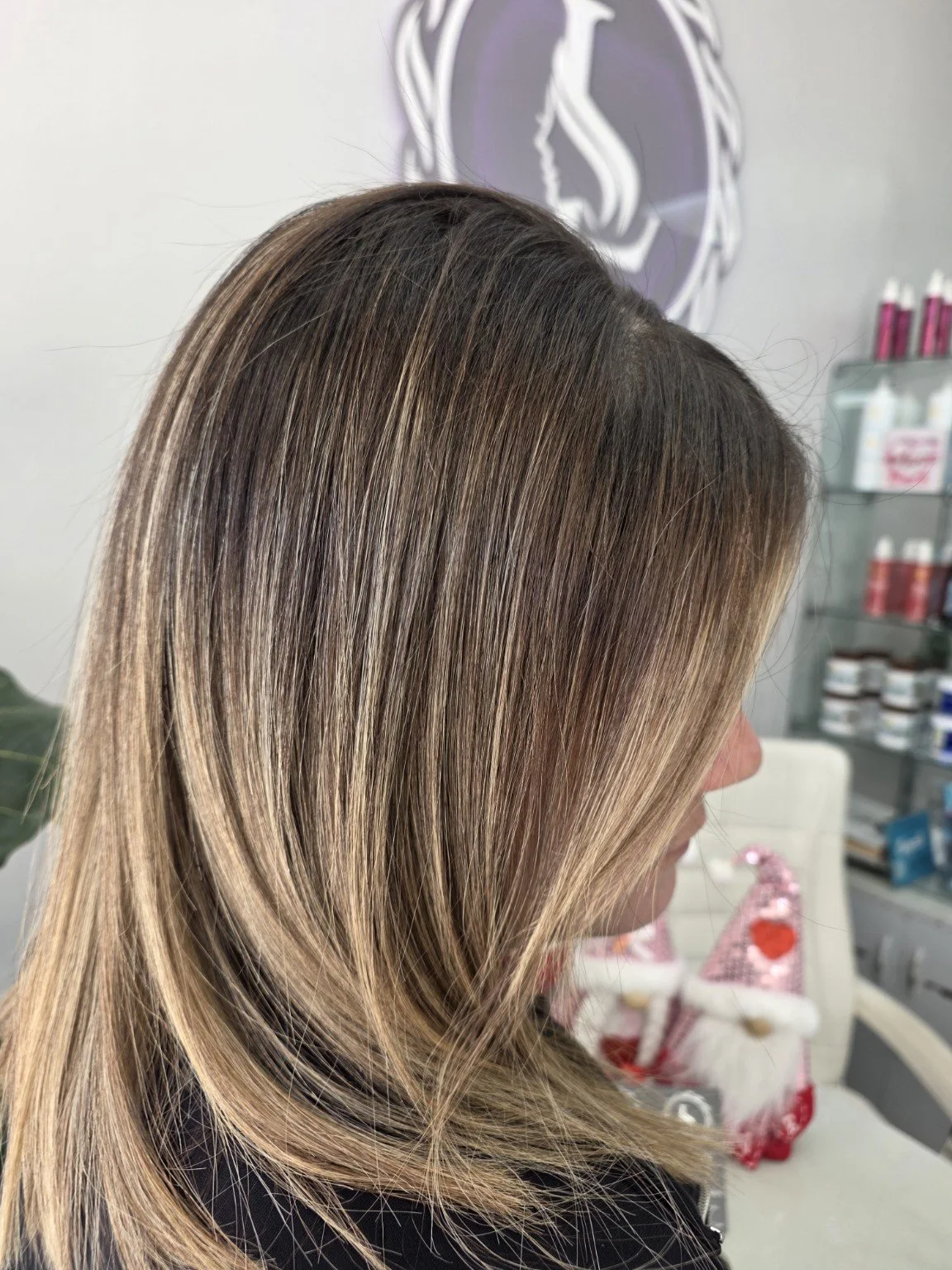 Side view of a woman with long, straight, blonde hair with darker roots, indoors in a salon.