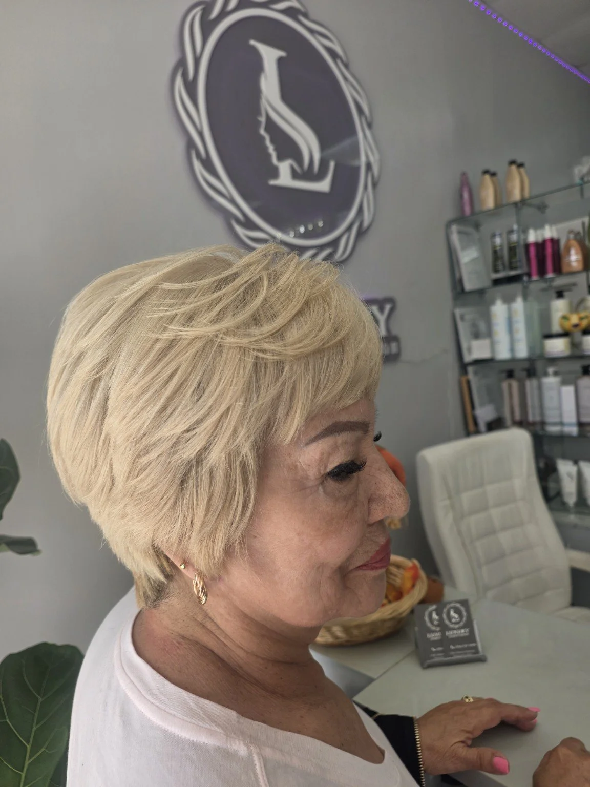 Older woman with blonde hair in a salon with a portrait of a woman with a braid in the background.