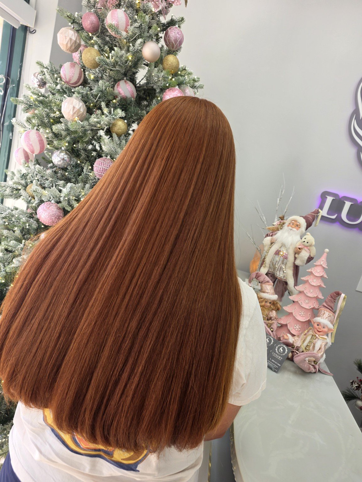 Back of a person with long, straight, red hair standing in front of a decorated Christmas tree and festive decorations.