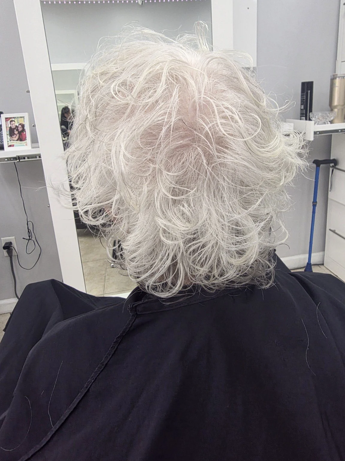 Back of a person with curly, light gray or white hair sitting in a salon chair.