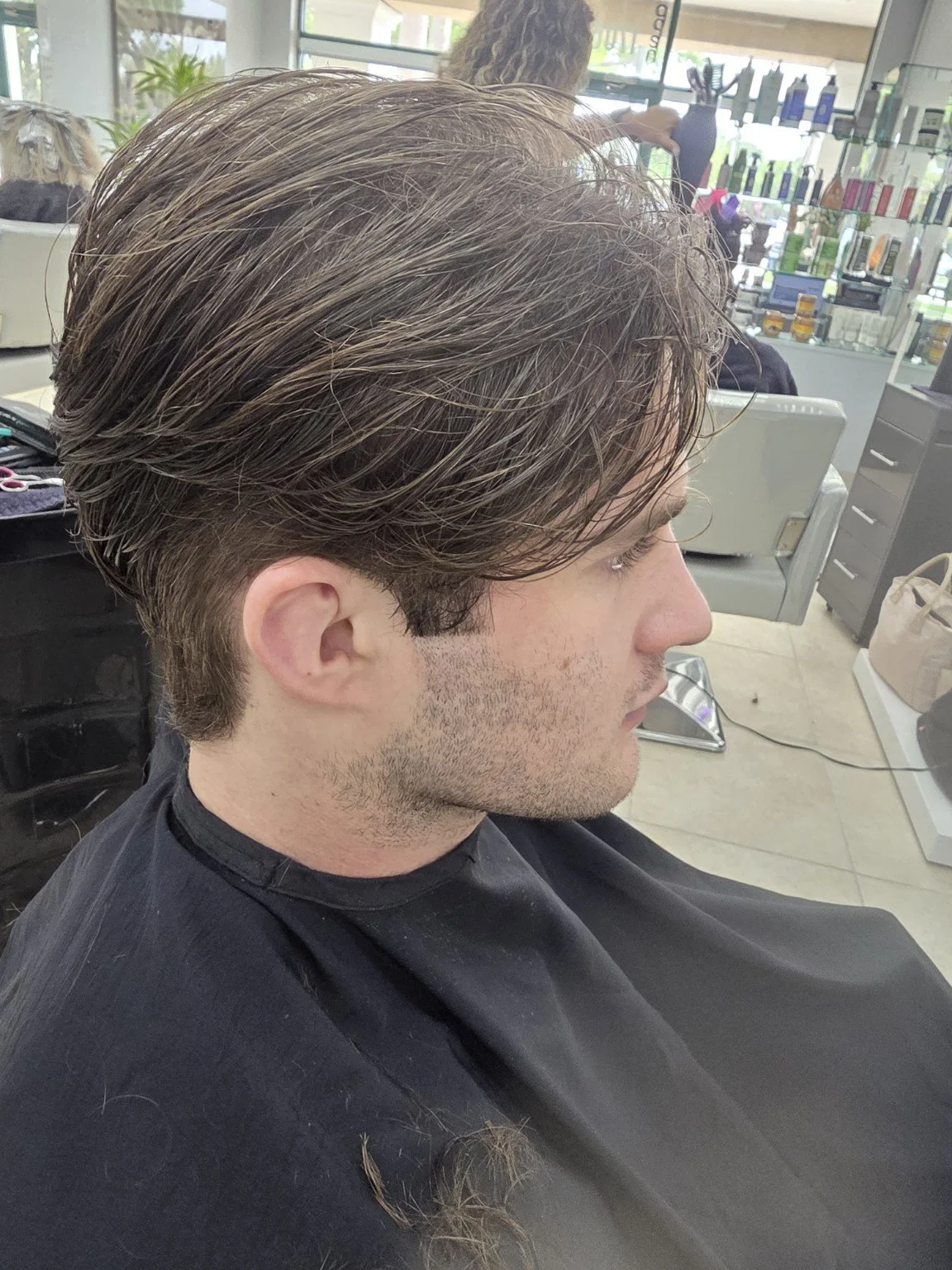 Side view of a man with styled brown hair getting a haircut at a salon.