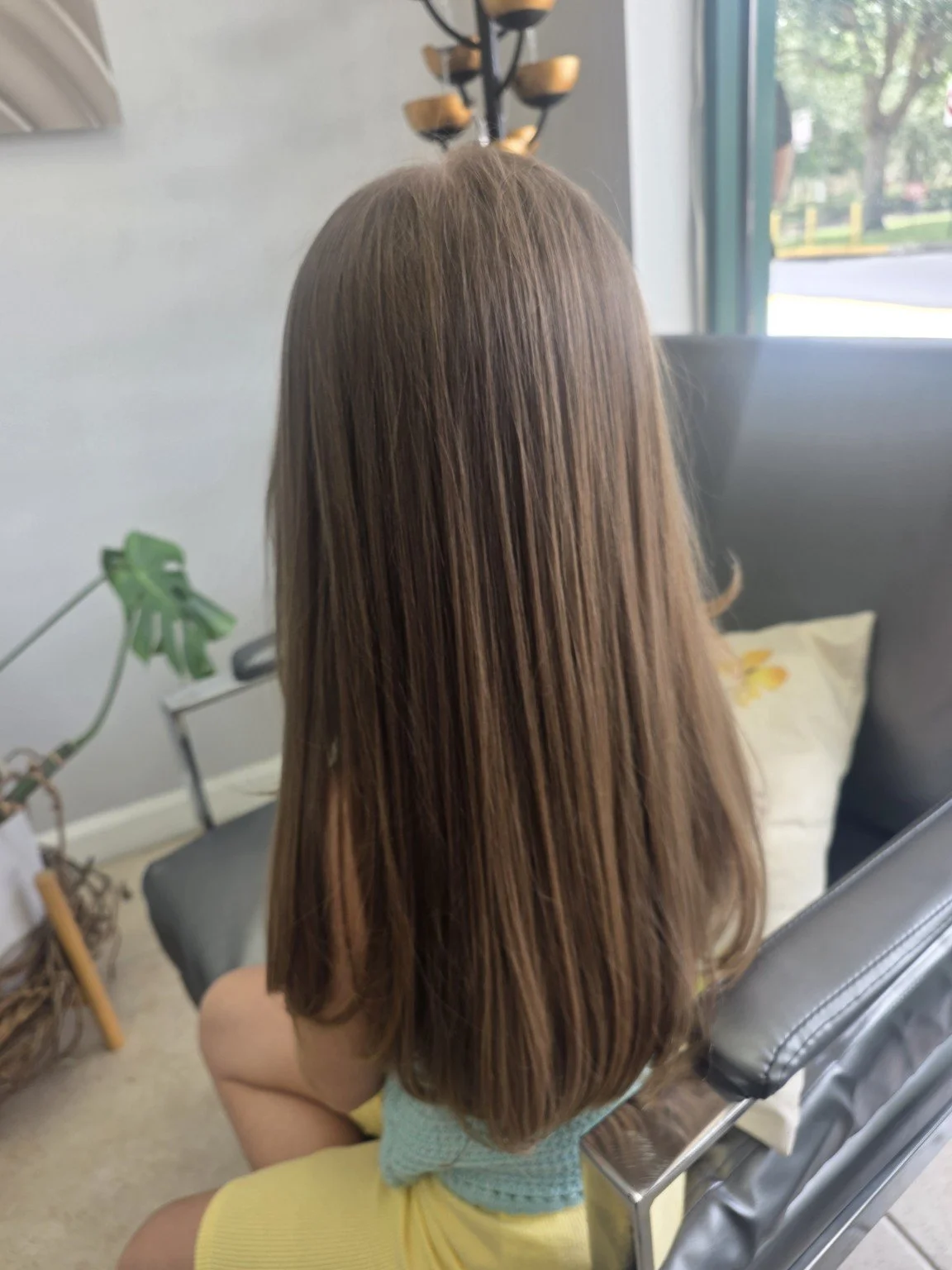 Woman with straight light brown hair sitting in a salon chair.