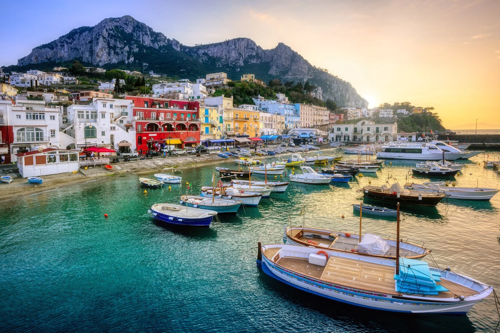 Colorful buildings along a waterfront with boats docked in the harbor at sunset