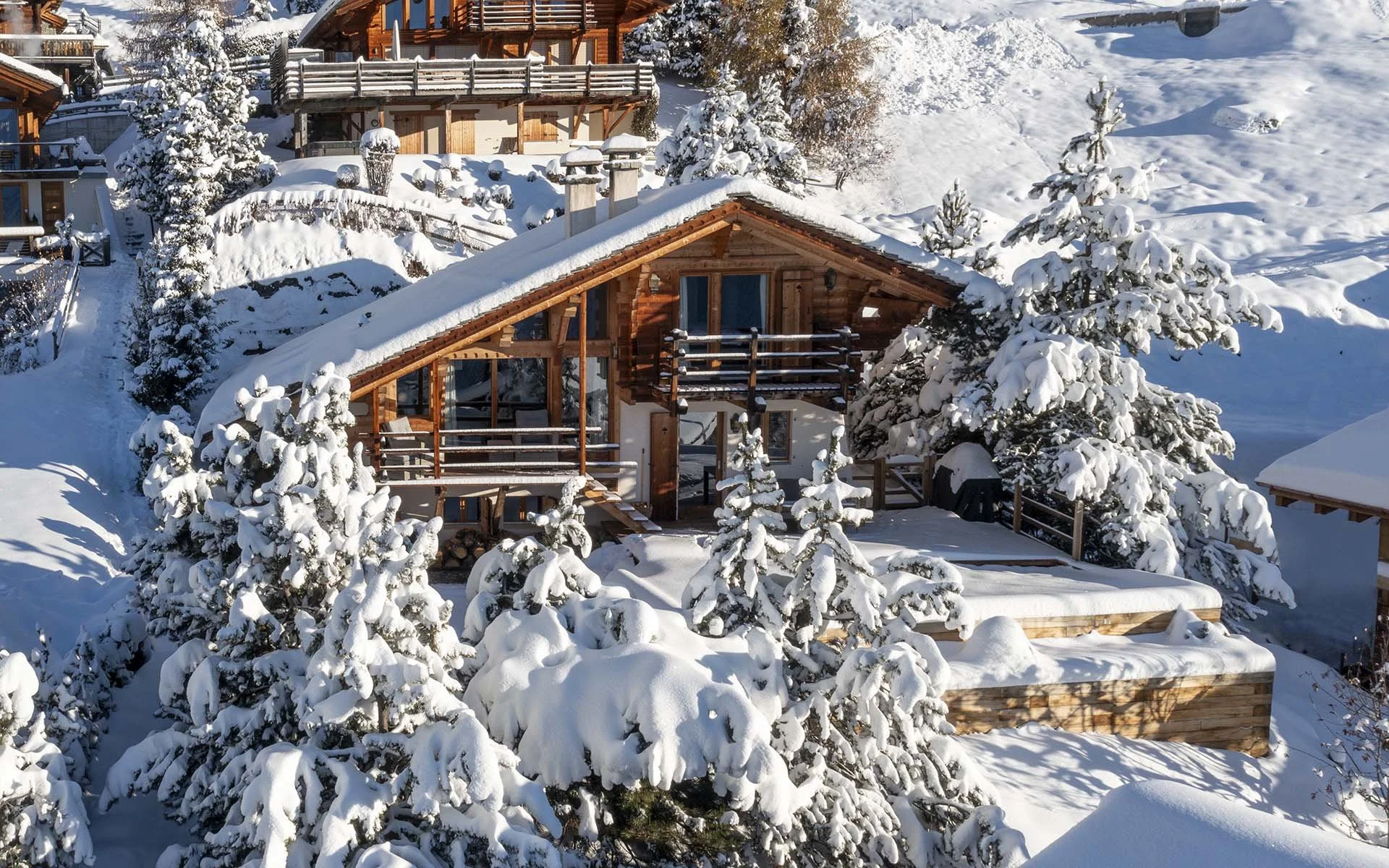 Snow-covered wooden houses and trees in a mountain chalet village.