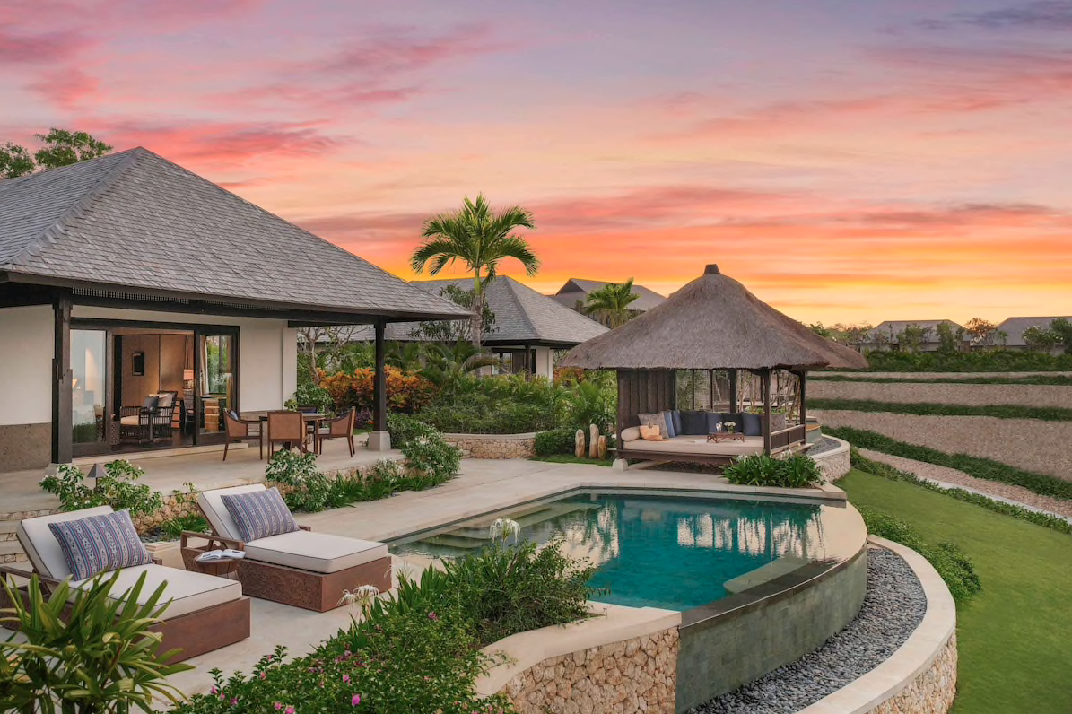 Luxury villa with a pool, tropical landscaping, and a thatched-roof gazebo at sunset.