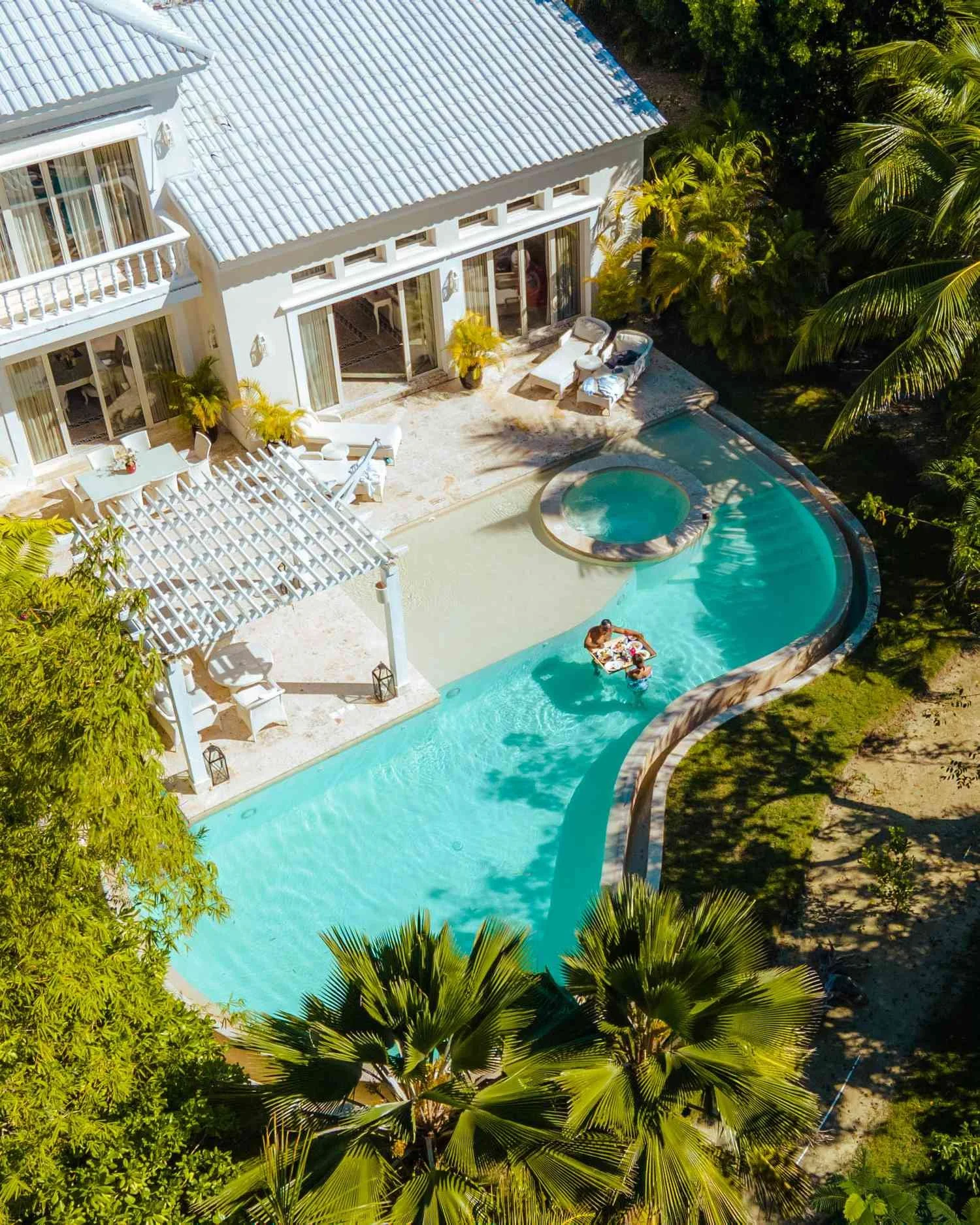 Aerial view of a white house with a swimming pool surrounded by lush green tropical trees.