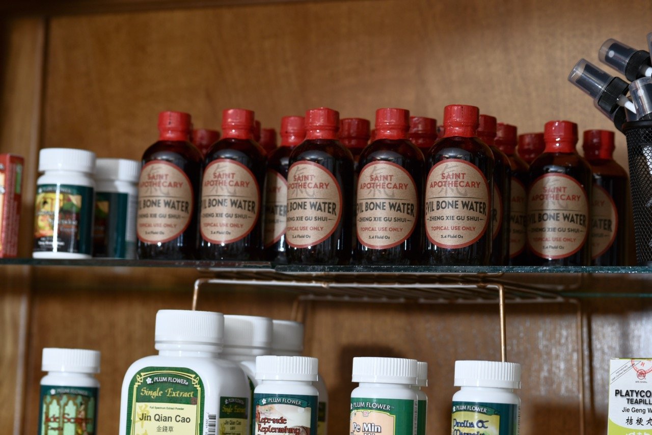 Shelf with bottles of herbal medicine and tinctures, including Saint Apothecary Evil Bone Water in small dark bottles with red caps.