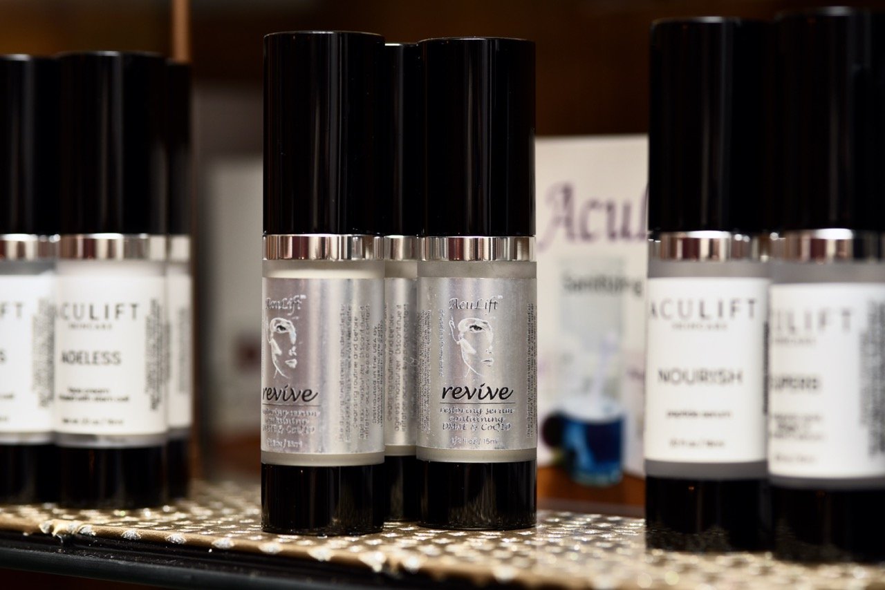 Black bottles of skincare products labeled 'Revive' with a logo of a face outline, displayed on a shelf.