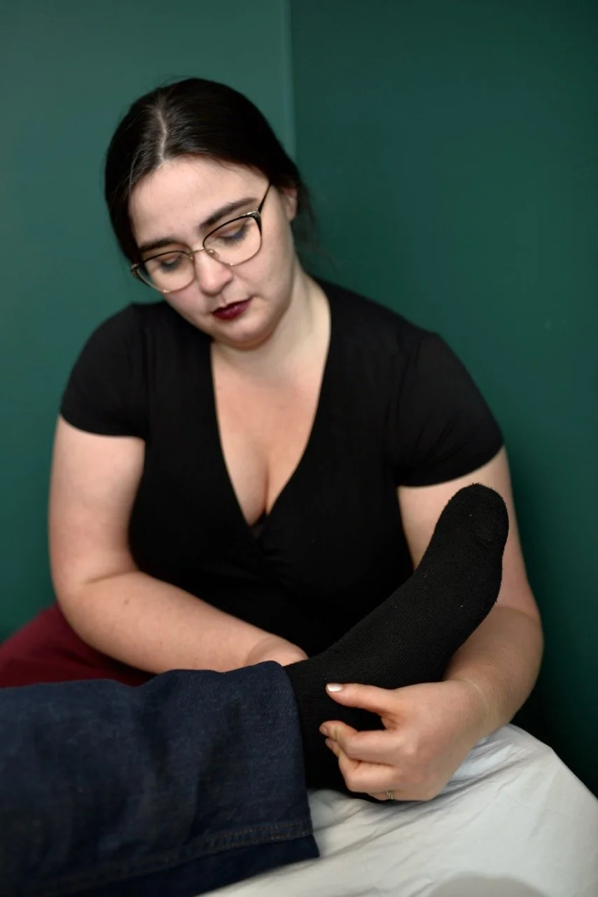 An acupuncturist performs nervous system regulation while holding a person's foot in a black sock.