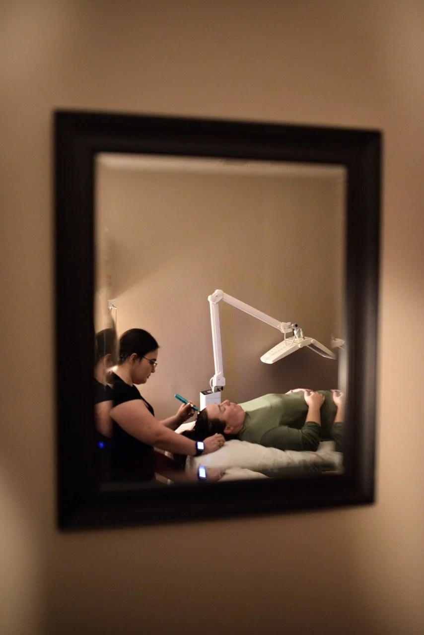 A woman lying on a treatment bed receiving a hair growth treatment, as seen through a mirror.