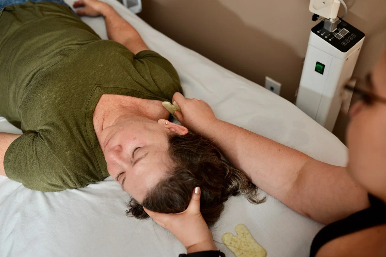 A person lying on a hospital bed with eyes closed, receiving care from a healthcare worker, with a stethoscope placed on their chest.