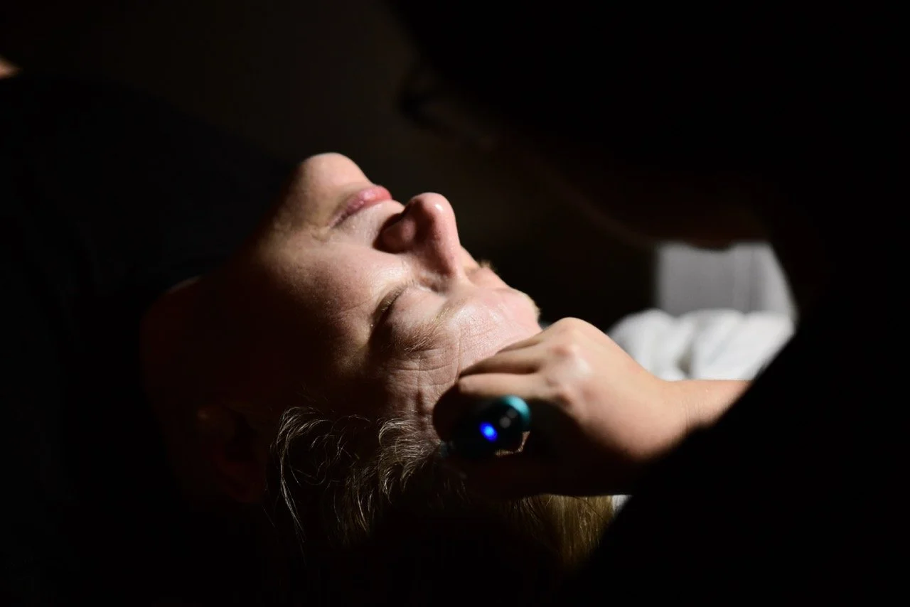 A woman receiving a facial treatment with a small device in a dimly lit room.