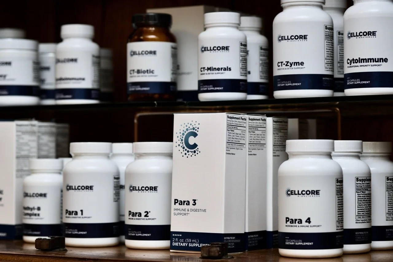 Various bottles of dietary supplements labeled 'Para 1,' 'Para 2,' 'Para 3,' and 'Para 4' on a wooden shelf, with some shelves holding additional supplements in bottles branded 'Cellcore.'