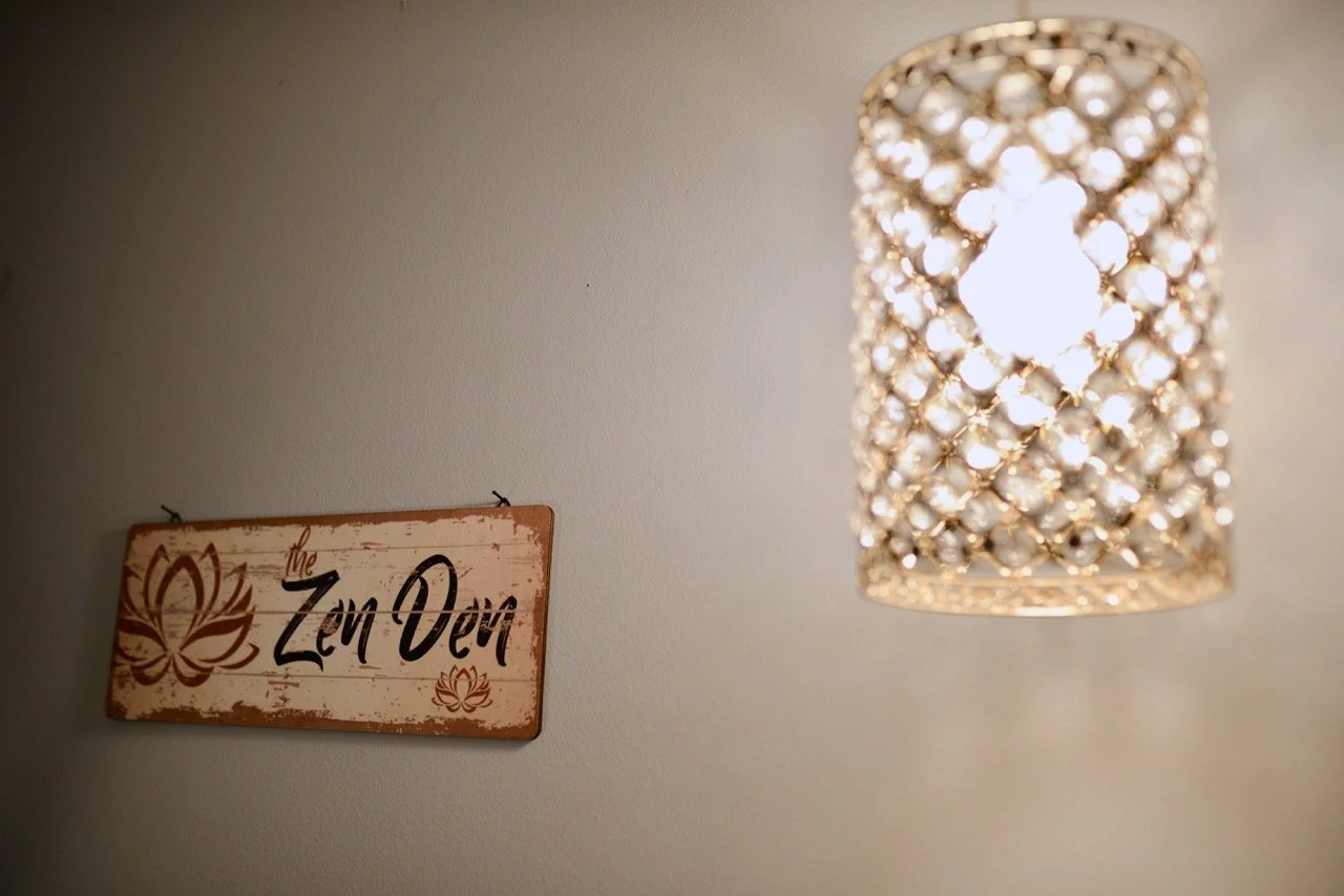 A wall sign that says 'The Zen Den' with lotus flower artwork and a hanging decorative light fixture with crystals.