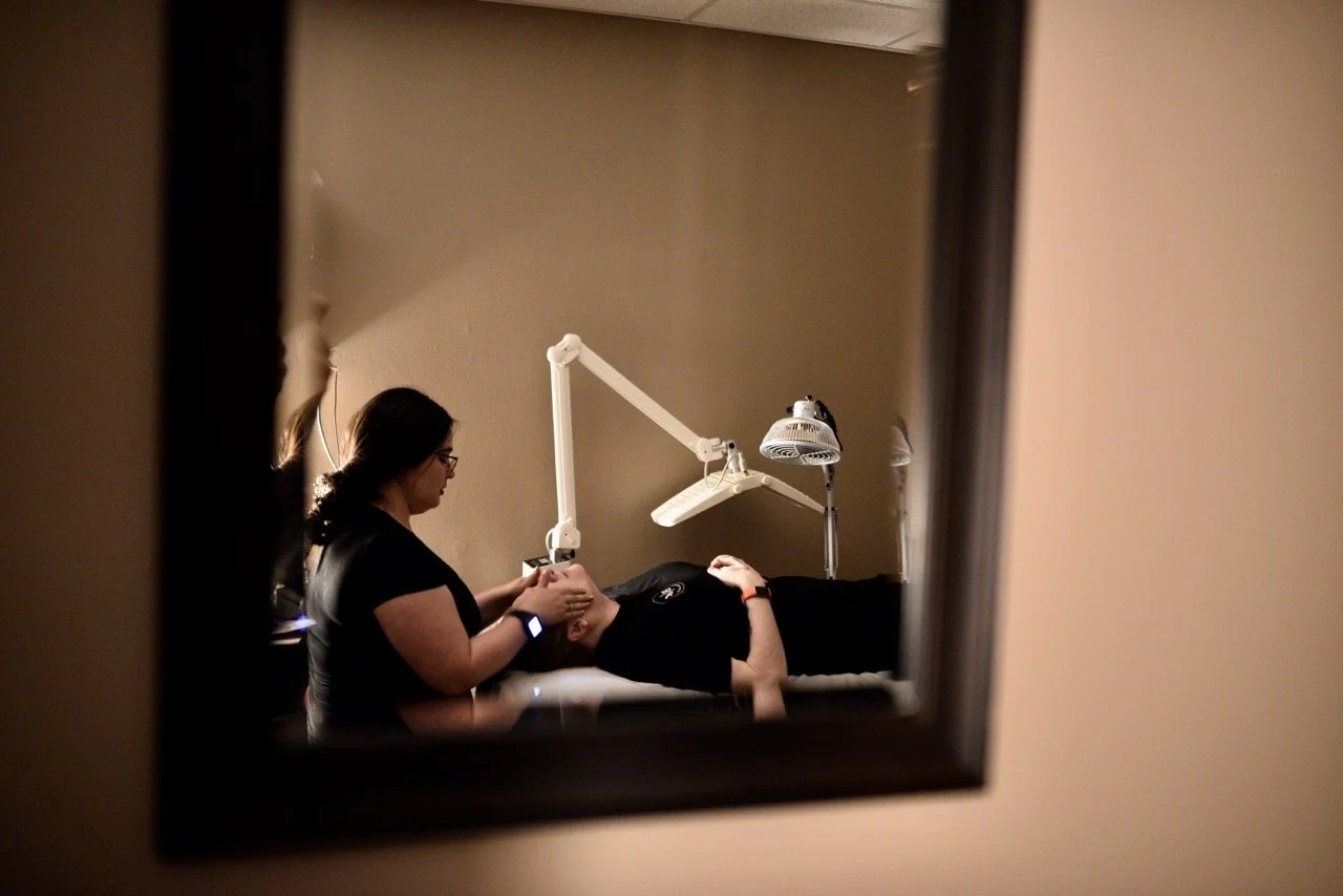 A woman receiving a facial treatment from a practitioner in Red Dragon Wellness clinic, viewed through a mirror.