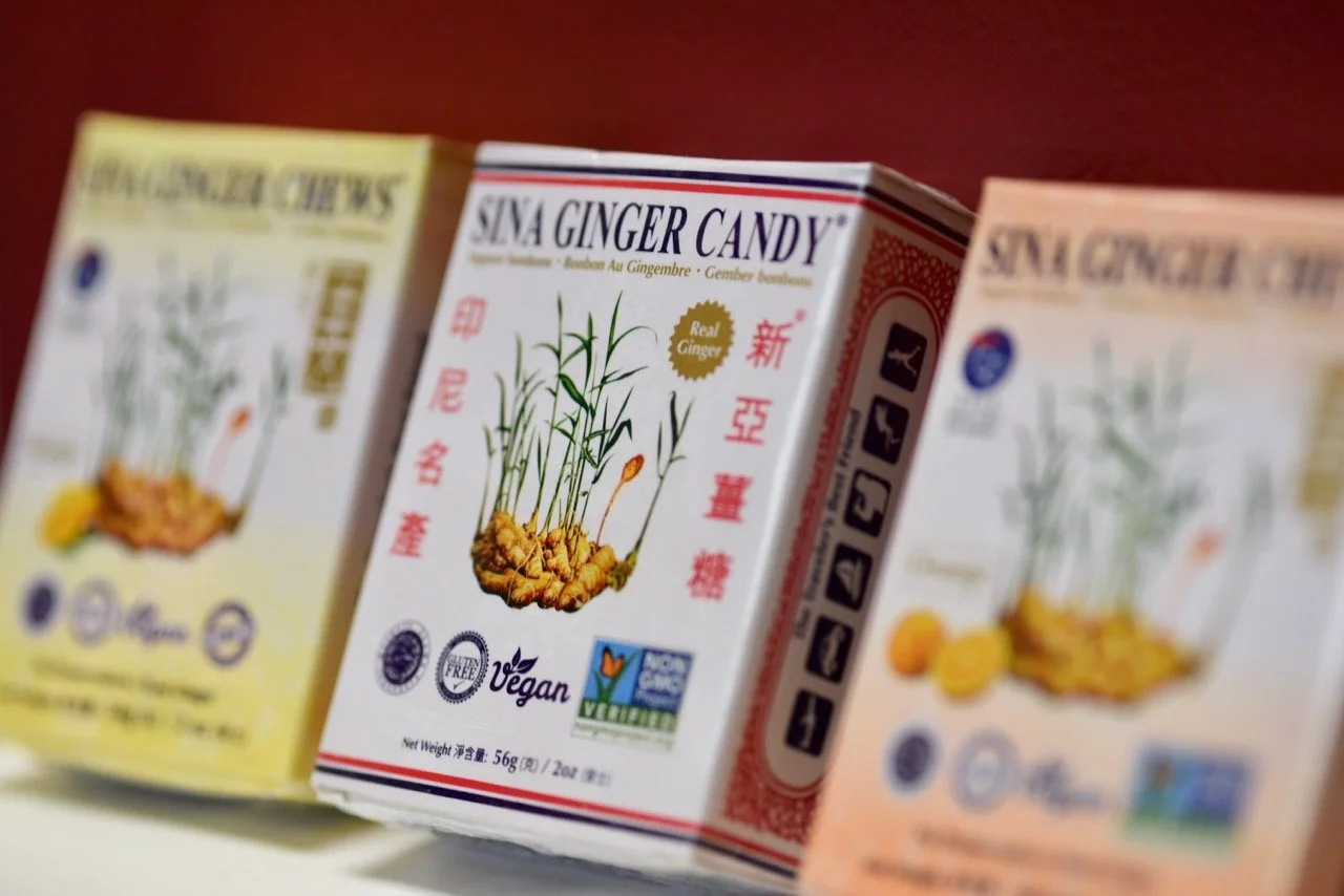 Close-up of three boxes of SN Ginger Candy, with one in the center showing bright and clear labeling, featuring ginger root illustrations and vegan certification symbols.