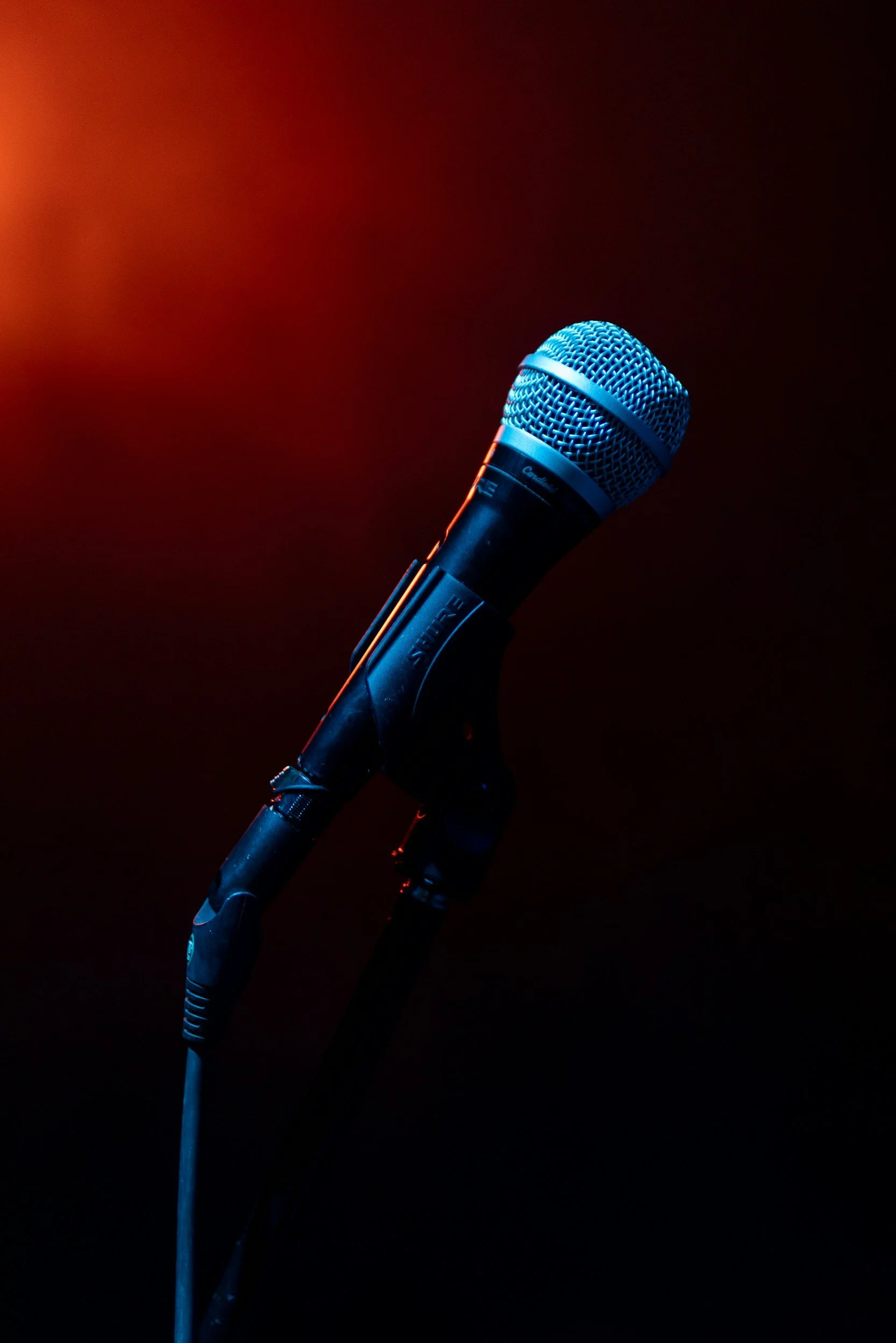 Close-up of a microphone on a stand, lit with blue and orange lighting, against a dark background.