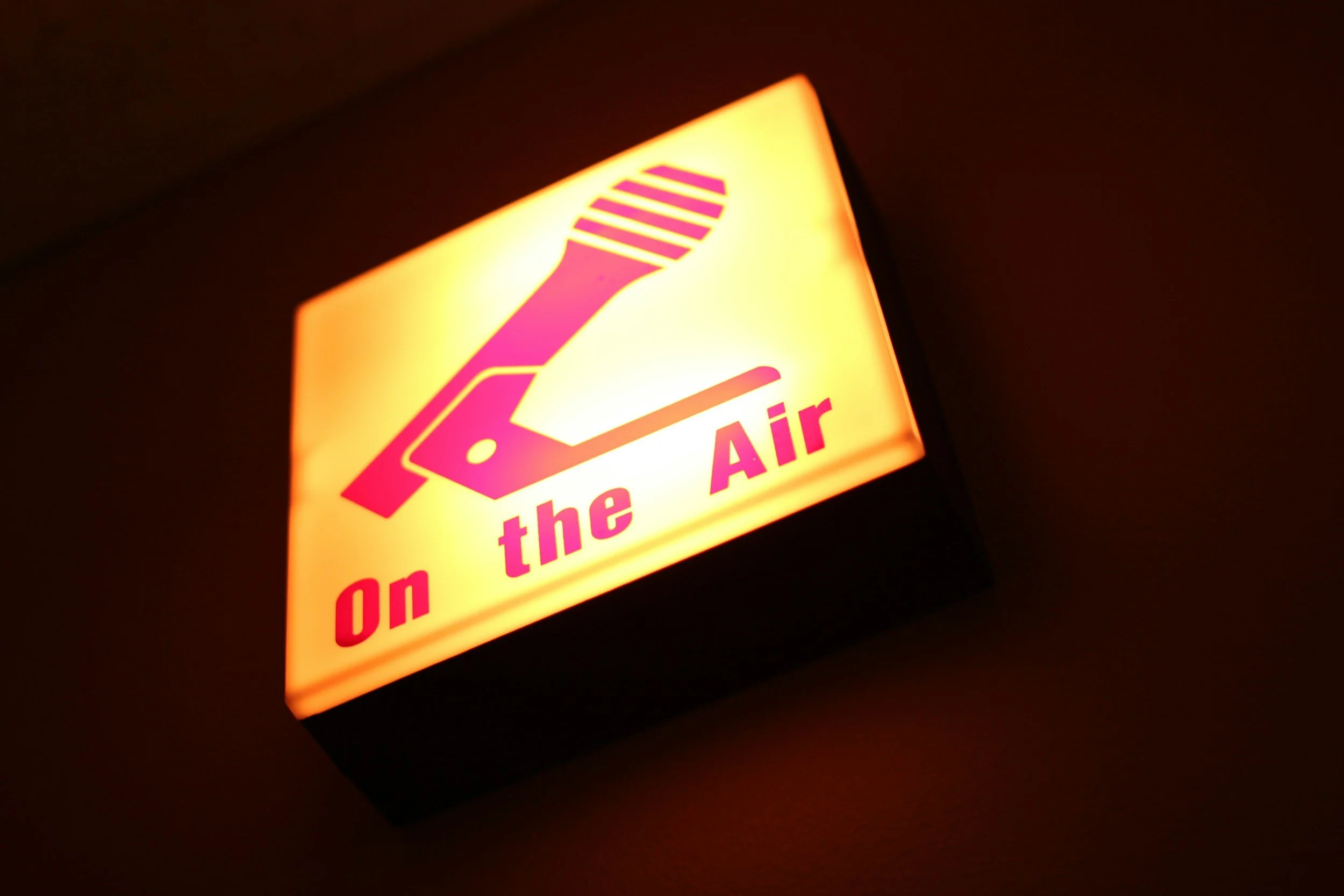 Illuminated sign with a pink and yellow design featuring a toothbrush and the text "On the Air" in pink.