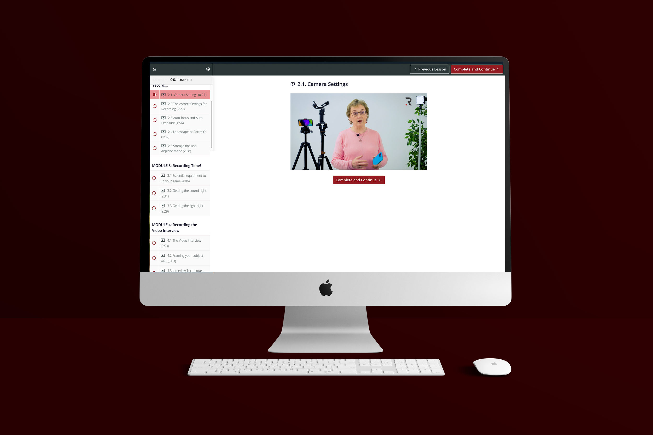 iMac computer with a keyboard and mouse on a red background, displaying an online course about camera settings, featuring a woman in a pink top explaining with camera equipment in the background.