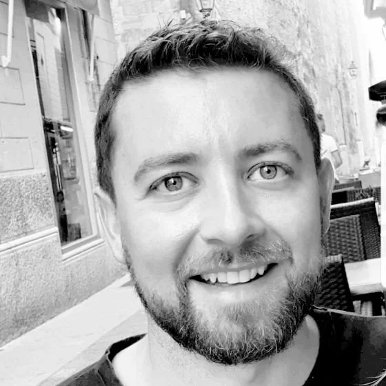 A smiling man with a beard and mustache posing outdoors in a black and white photo.