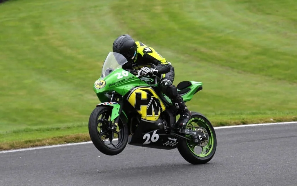 A motorcycle with a racer performing a wheelie on a race track, green and black in color with racing number 26.
