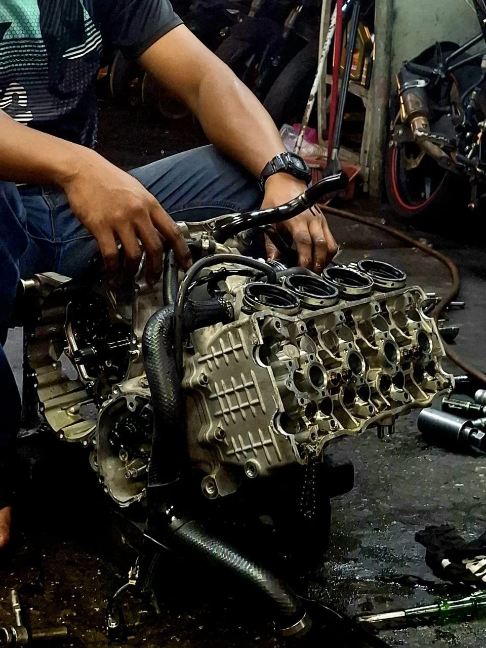 Person working on a motorcycle engine in a workshop, with various tools and motorcycle parts visible in the background.