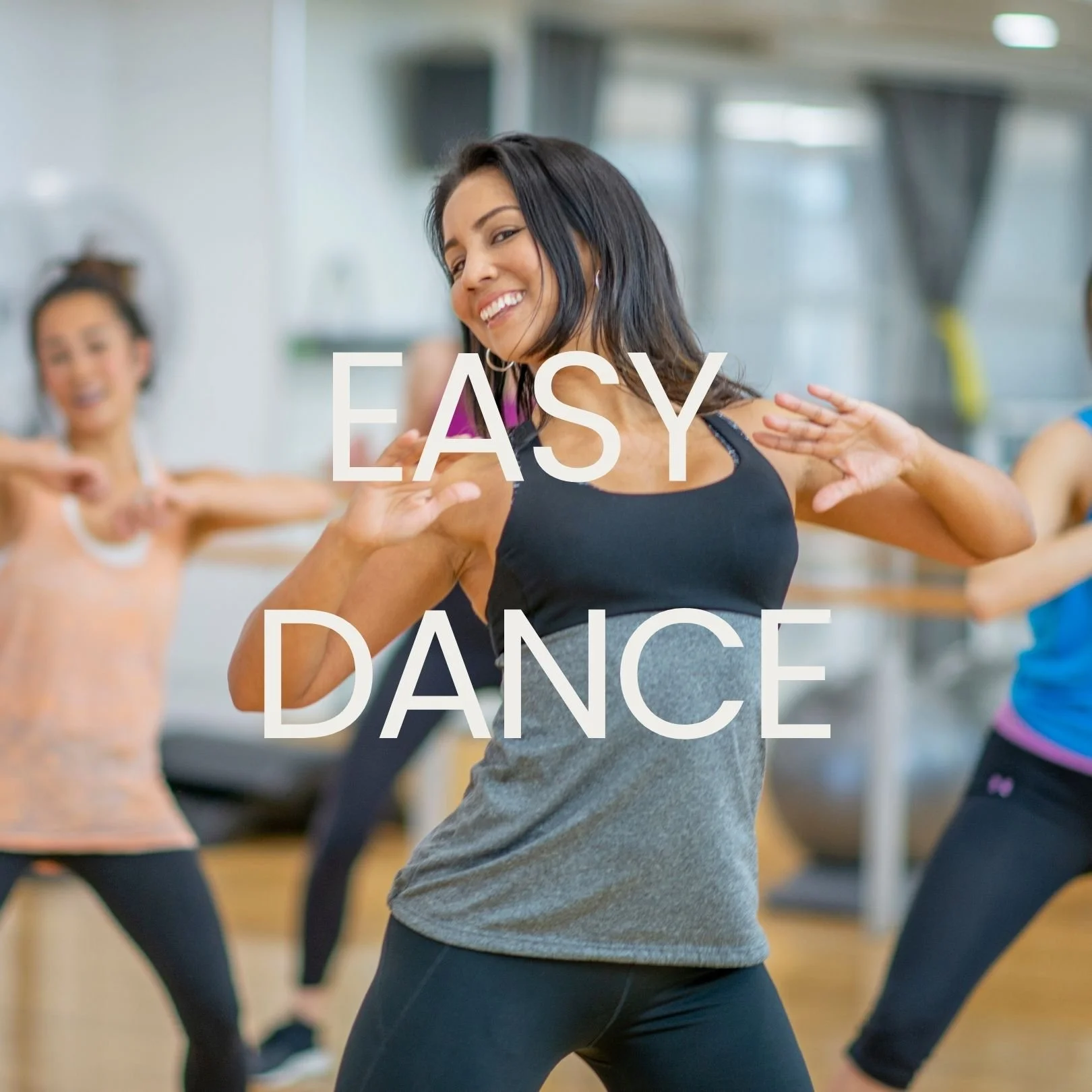 A woman leading a dance class with a smile while nearby women follow her dance moves in a fitness studio.