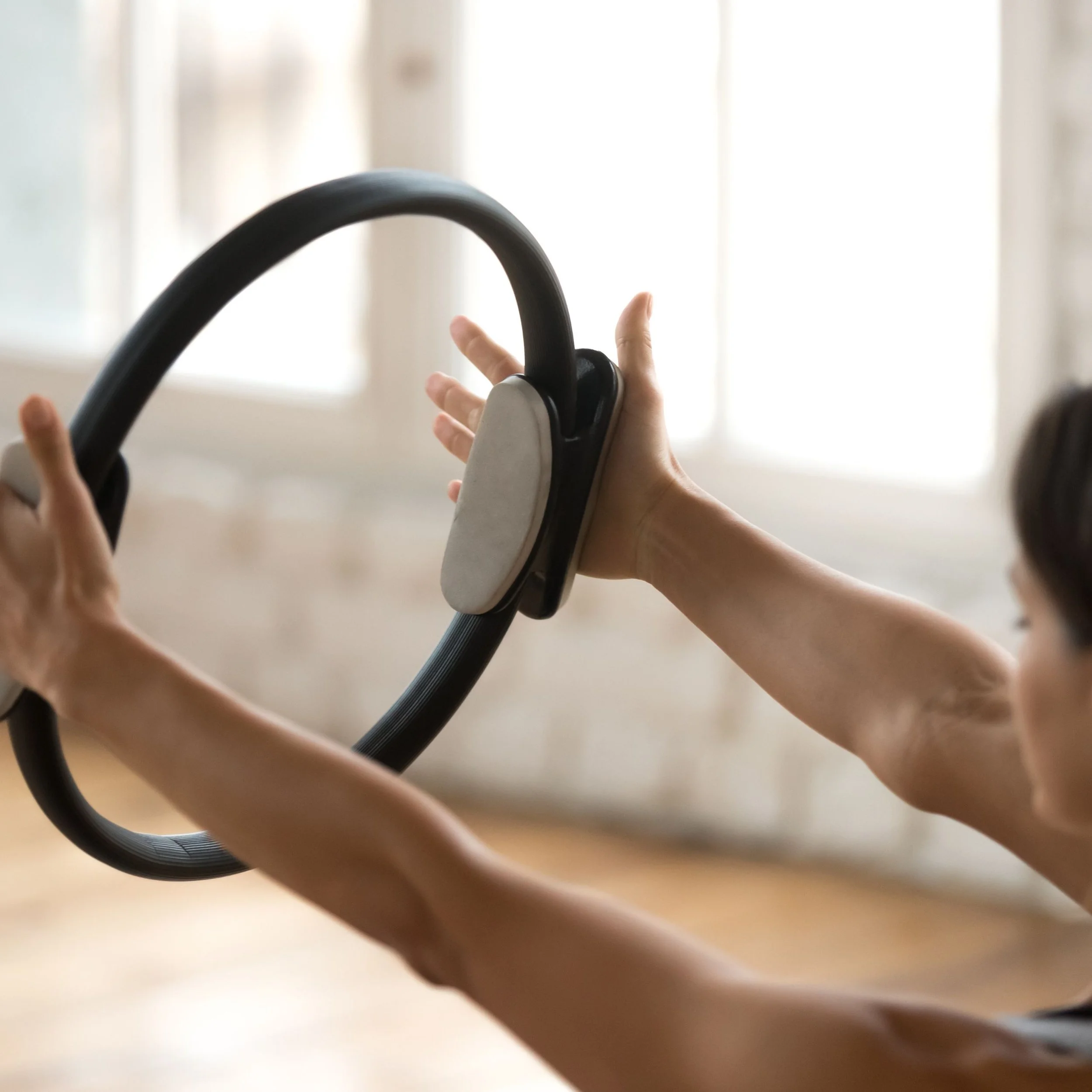 Person exercising with a Pilates ring in a bright room.