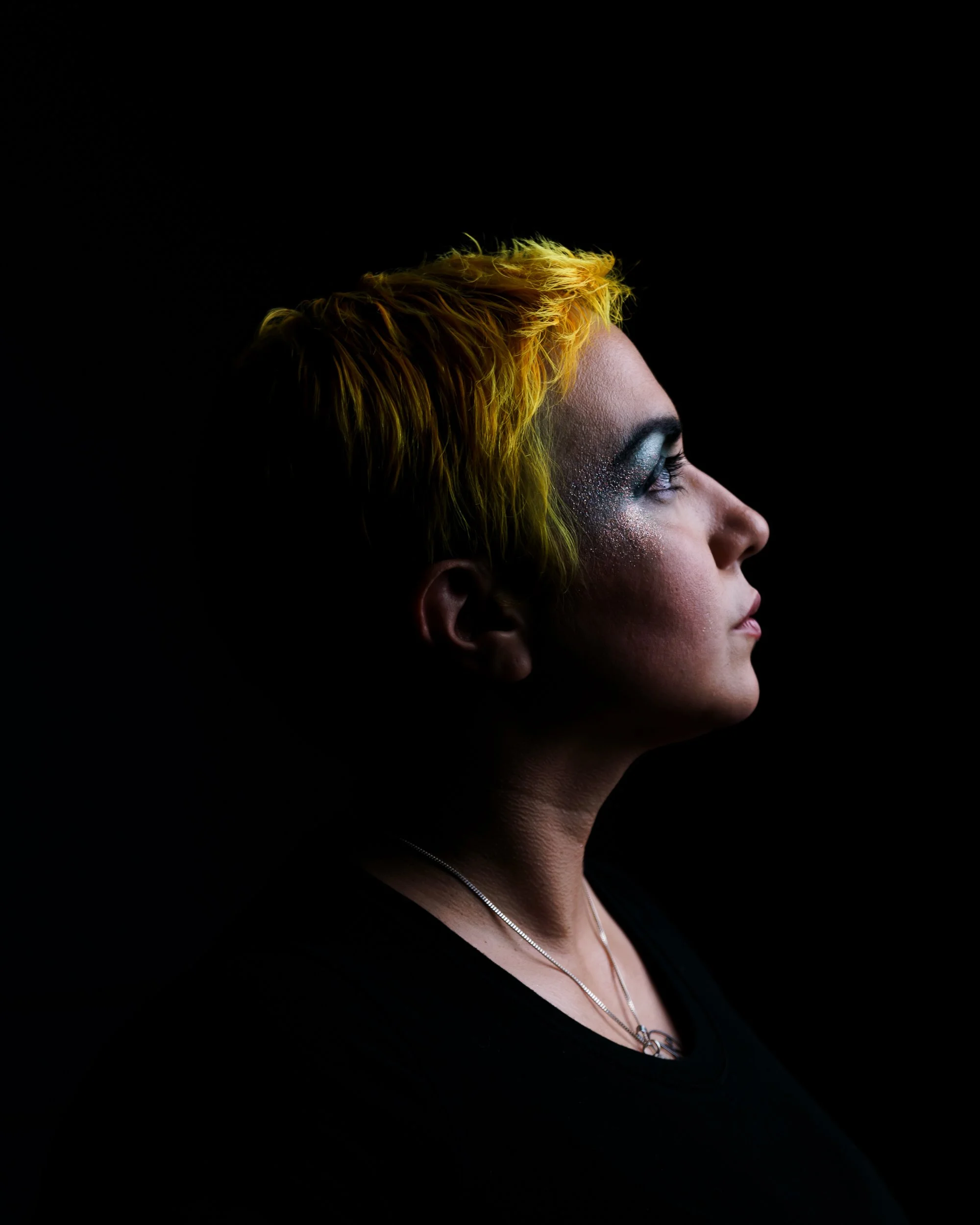 Musician Nina Diaz leans into a microphone mid-song, her face lit by stage light in a dim performance venue.