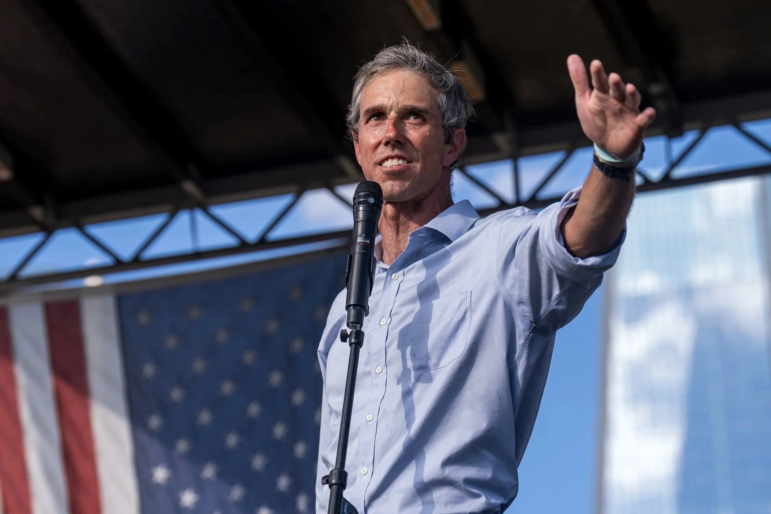 Beto O’Rourke speaks from a stage, gesturing with his hand as an American flag hangs behind him during the “No Kings” rally in San Antonio, Texas.