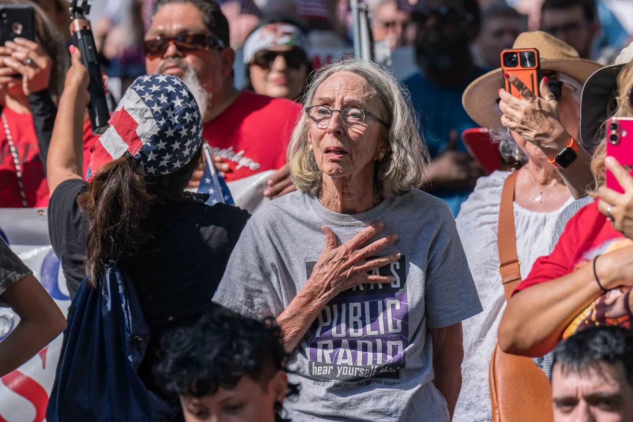 A woman wearing a "Public Radio" T-shirt places her hand over her heart during the national anthem at the "No Kings" protest in San Antonio, Texas, on June 14, 2025, part of nationwide protests opposing Trump administration immigration policies.