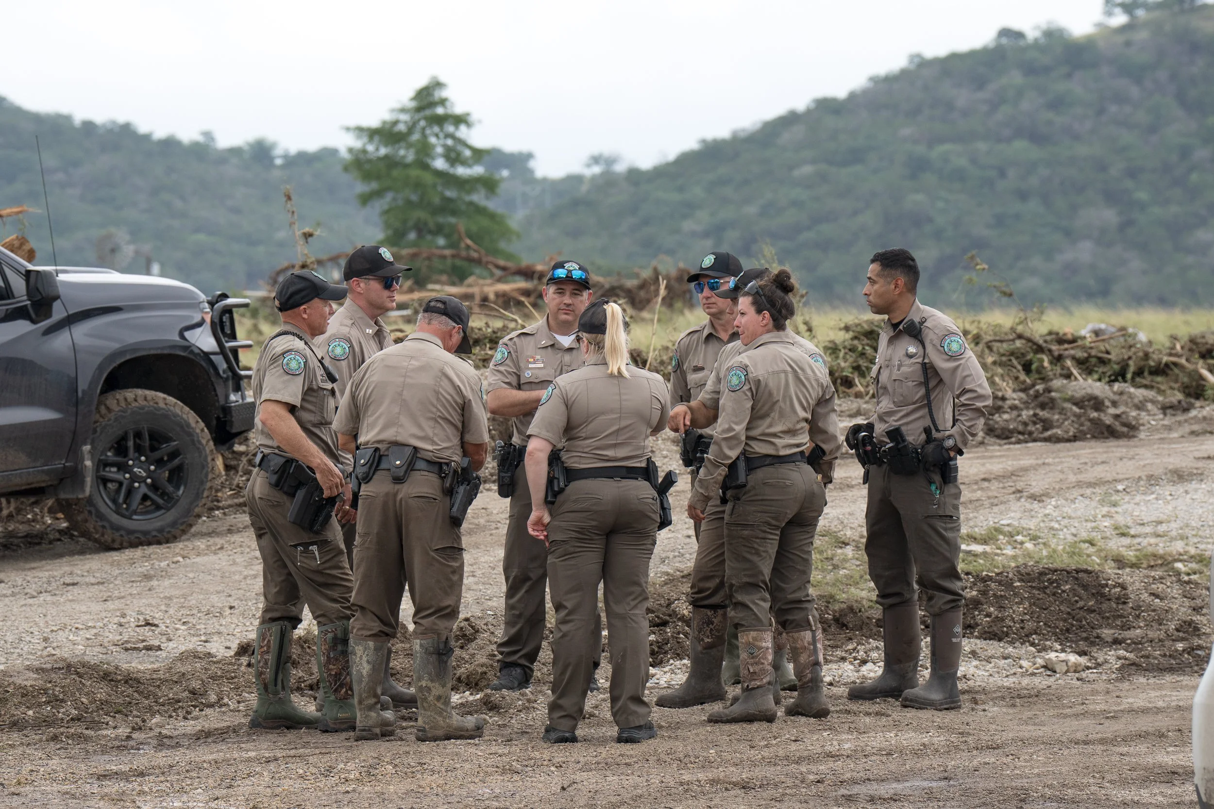Texas game wardens and local law-enforcement officers stand coordinating search and recovery efforts along the Guadalupe River.