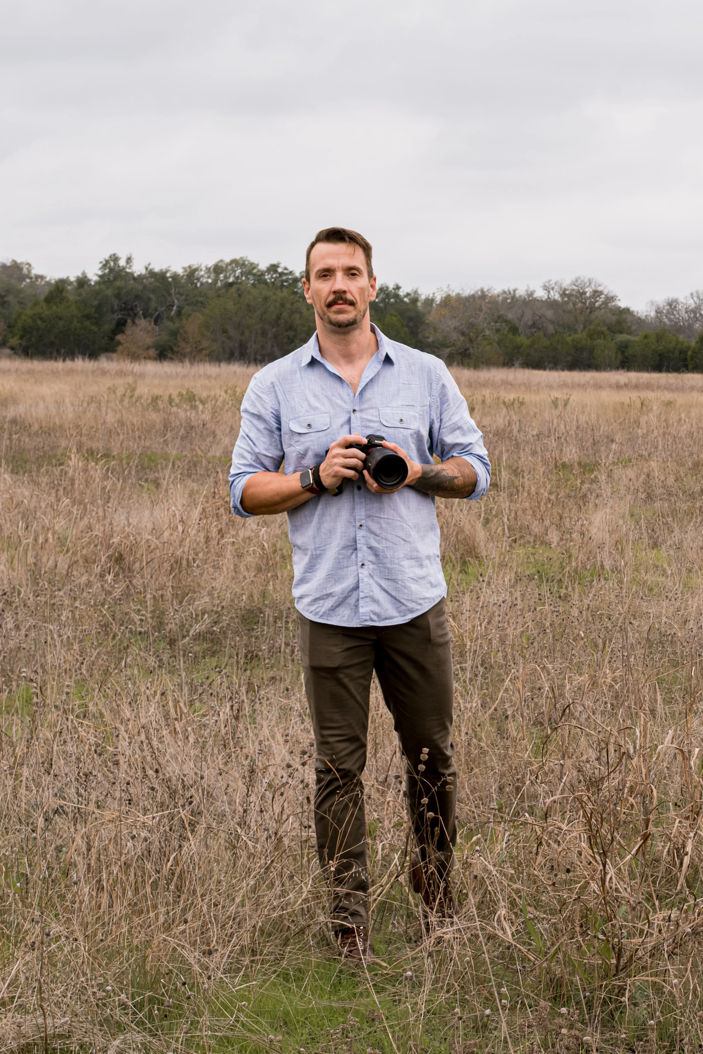 Photojournalist Eric Vryn holding a camera in a grassy Central Texas field under a cloudy sky.
