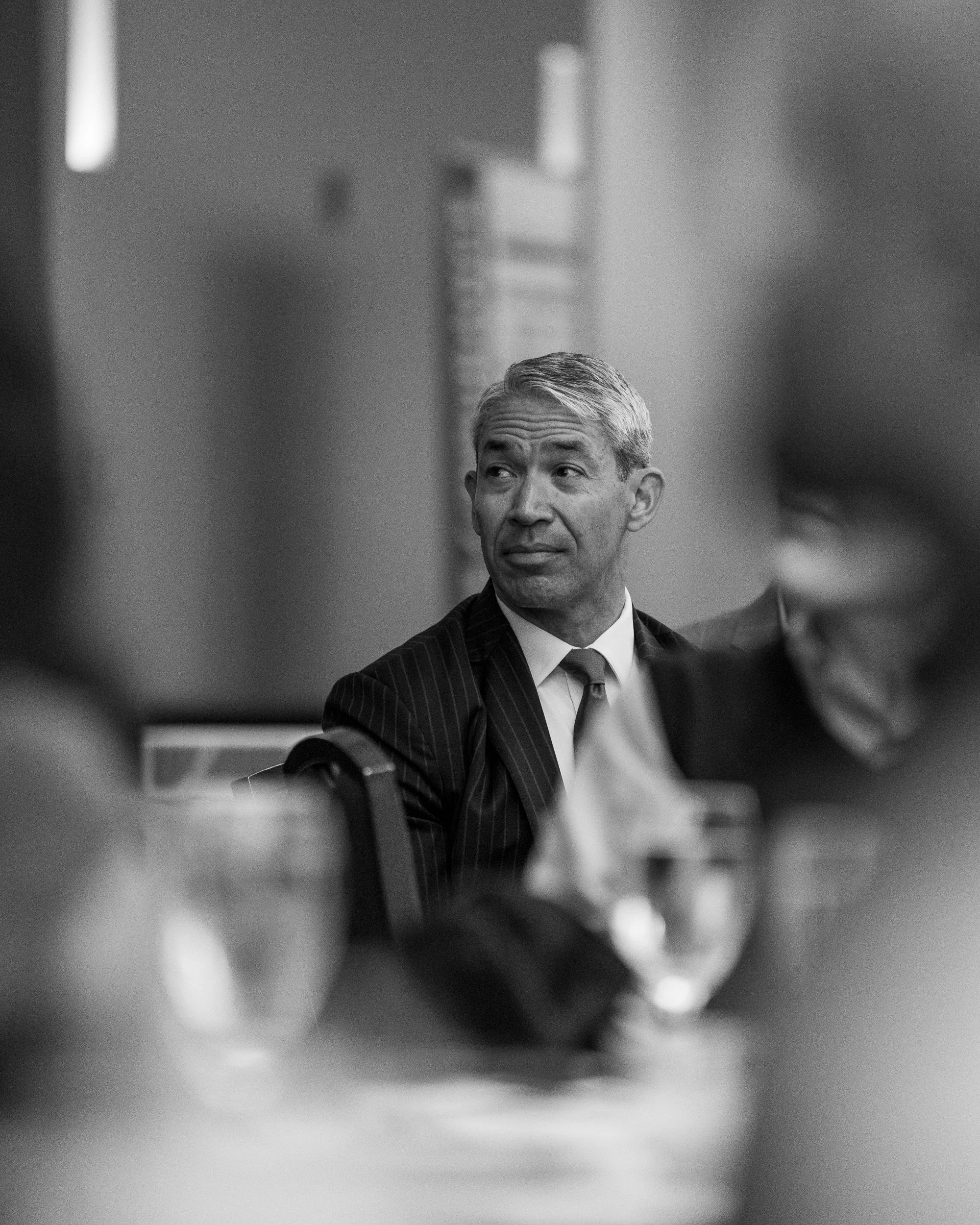 San Antonio Mayor Ron Nirenberg, in a pinstripe suit and tie, looks to his left while seated at a banquet table during a community event.