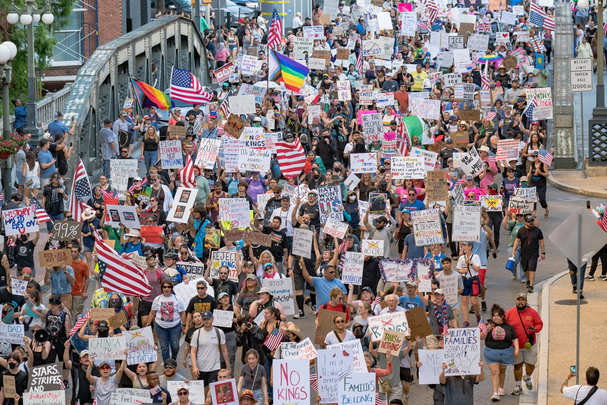 Thousands of protesters carrying signs and American flags march down Navarro Street during the "No Kings" demonstration in San Antonio, Texas, on June 14, 2025, part of nationwide protests opposing Trump administration immigration policies.