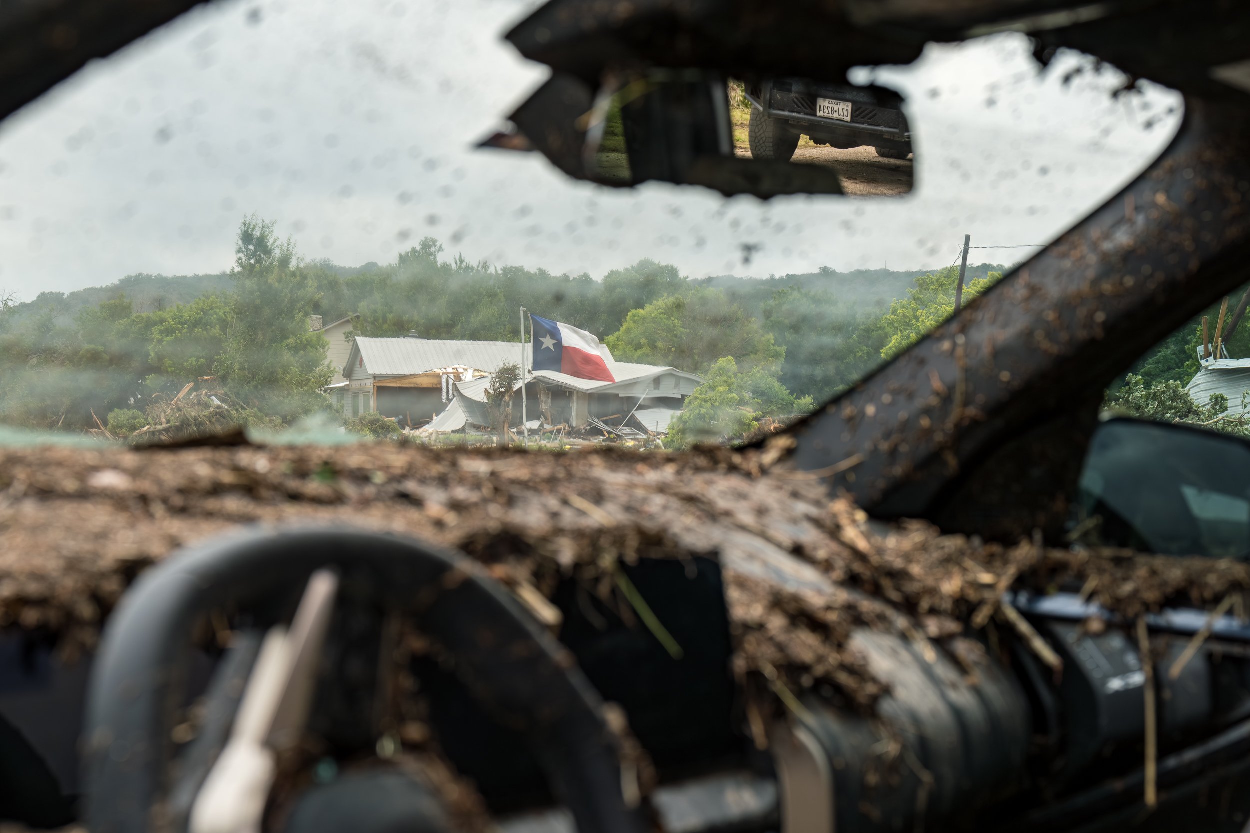 A Texas flag outside a damaged home is seen through the mud-caked interior of a vehicle destroyed by flooding along the Guadalupe River near Hunt, Texas, on July 5, 2025, after heavy rainfall triggered deadly flash flooding across Central Texas.