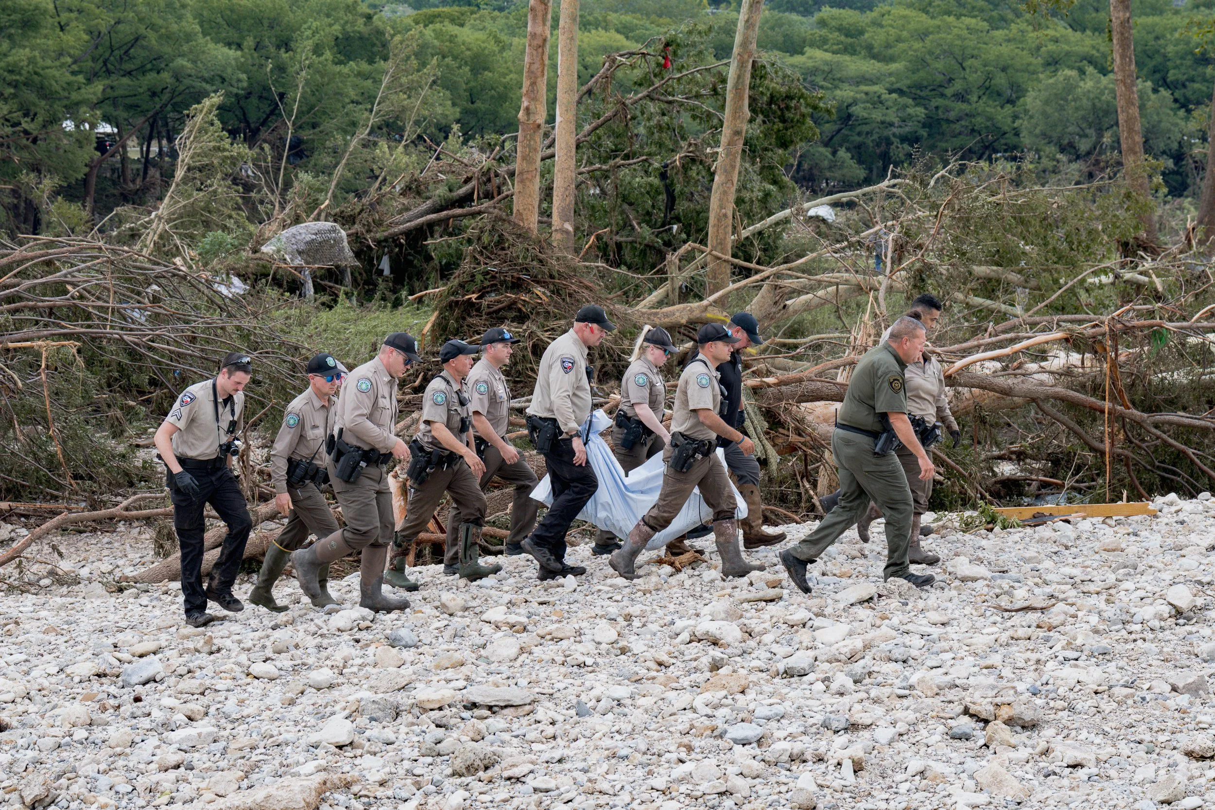 Texas game wardens and local law enforcement officers carry the body of a flood victim from the banks of the Guadalupe River during recovery operations in Hunt, Texas, on July 5, 2025, after heavy rainfall triggered deadly flash flooding across Centr