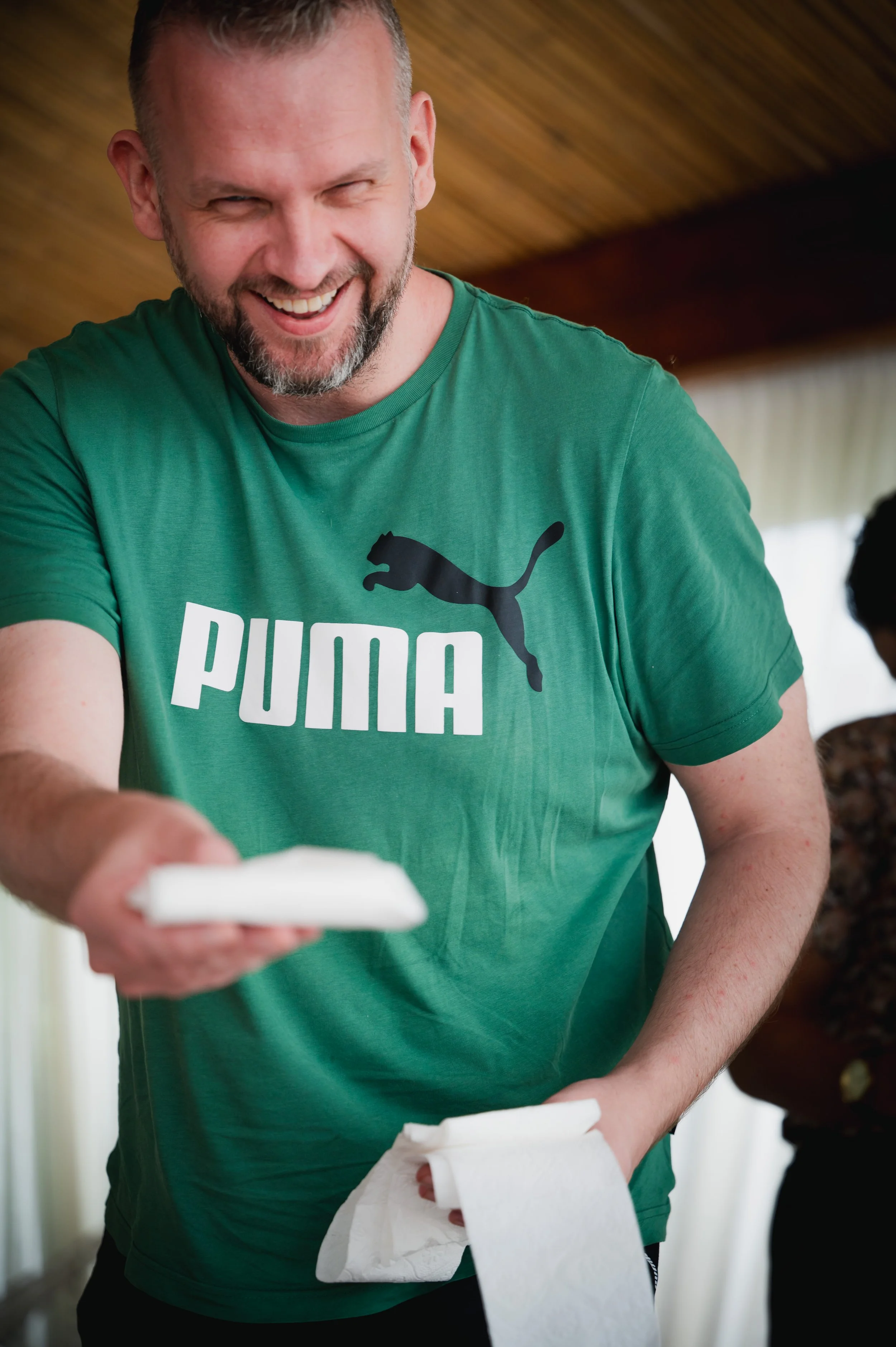 A man wearing a green Puma t-shirt is smiling and holding a napkin in a casual setting.