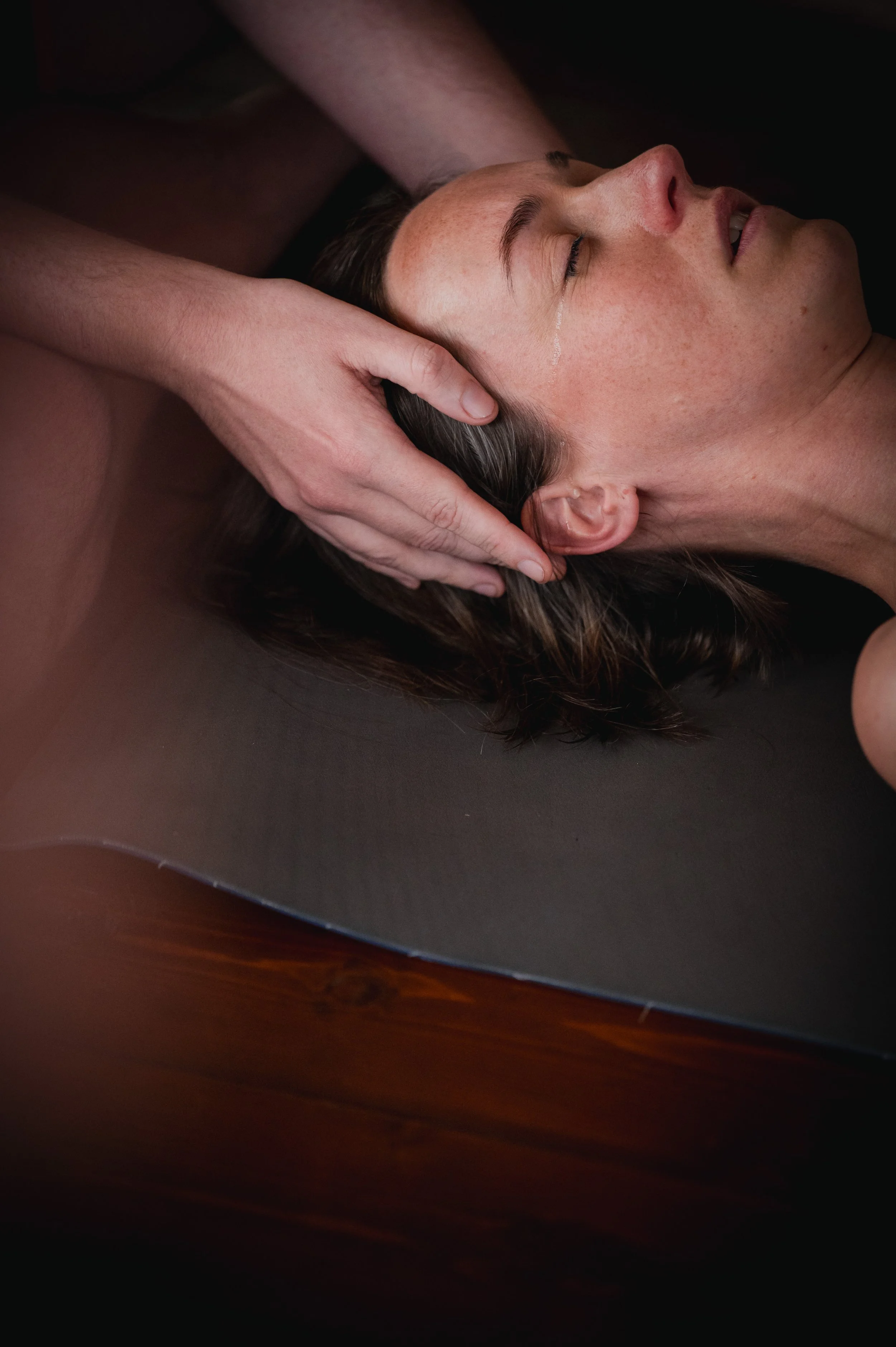 A woman receives a head massage while lying on a massage table with her eyes closed.