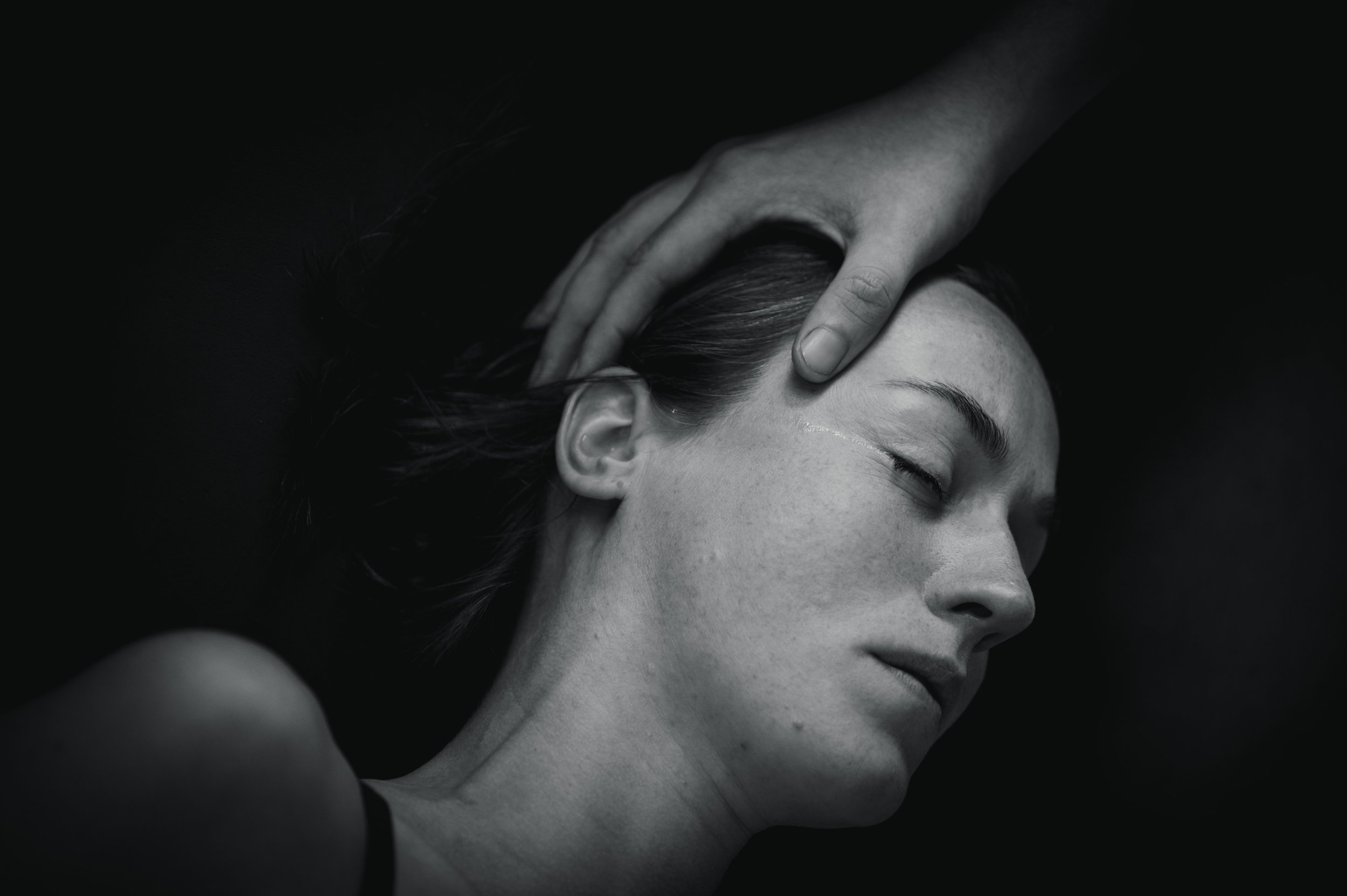 A woman receiving a massage with a closed eye, dark background