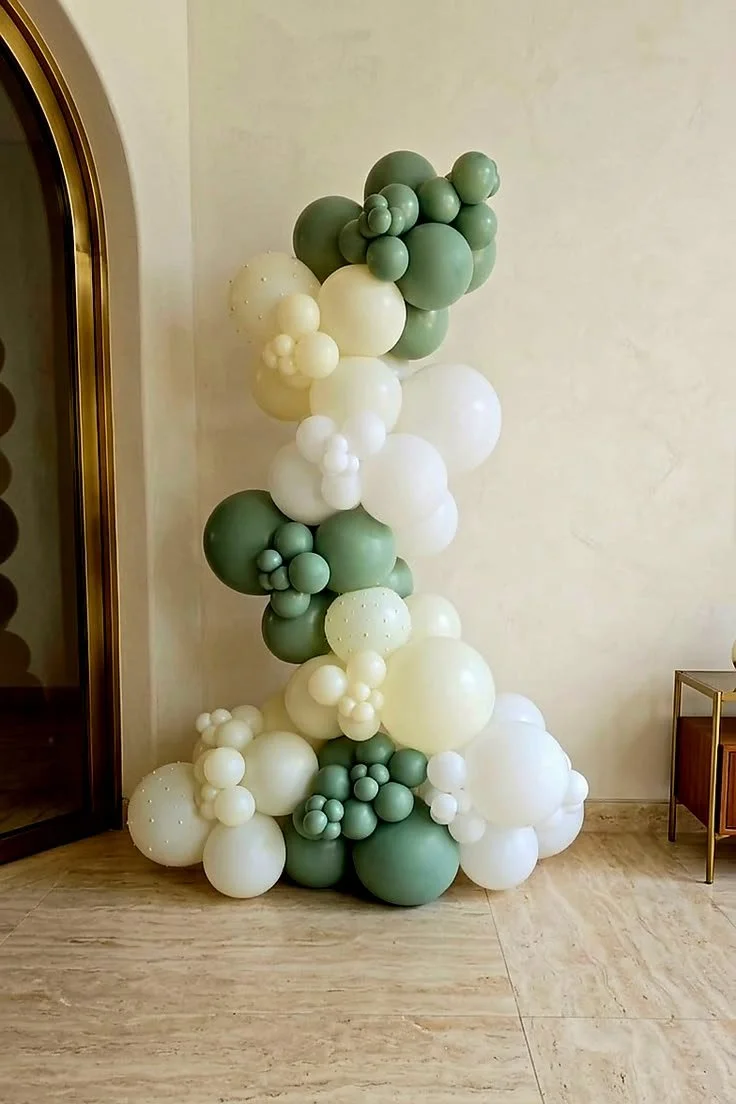 Organic floor-to-ceiling balloon garland column featuring eucalyptus green, cream, white, and pearl-textured balloons of various sizes in an elegant indoor setting.