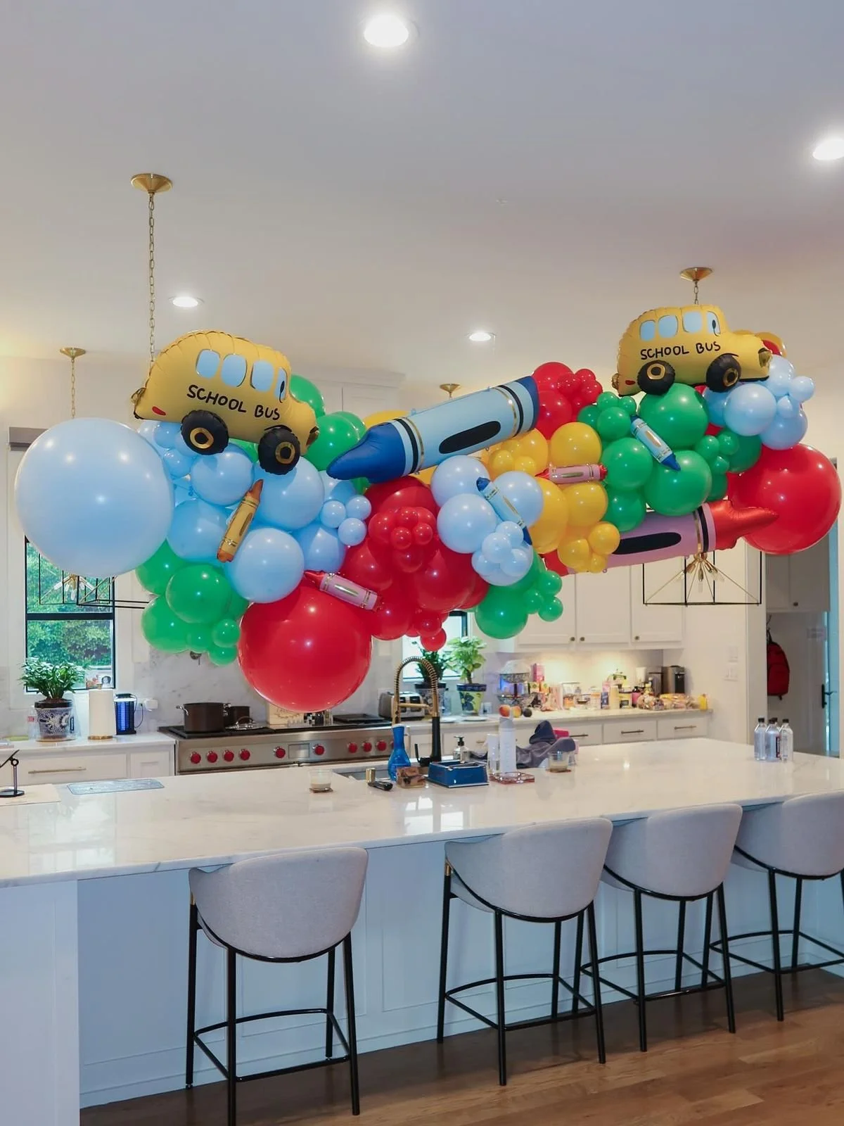 Colorful balloon decoration with school bus, pens, and clouds over a kitchen island.