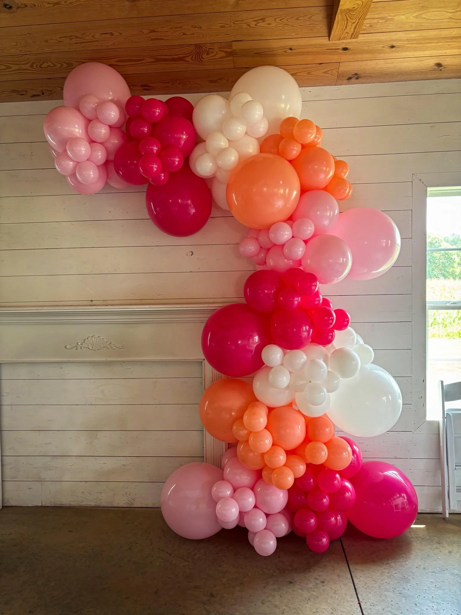 Graduation party balloon garland installation featuring bright pink, baby pink, white, and coral balloons for event decoration in Omaha.