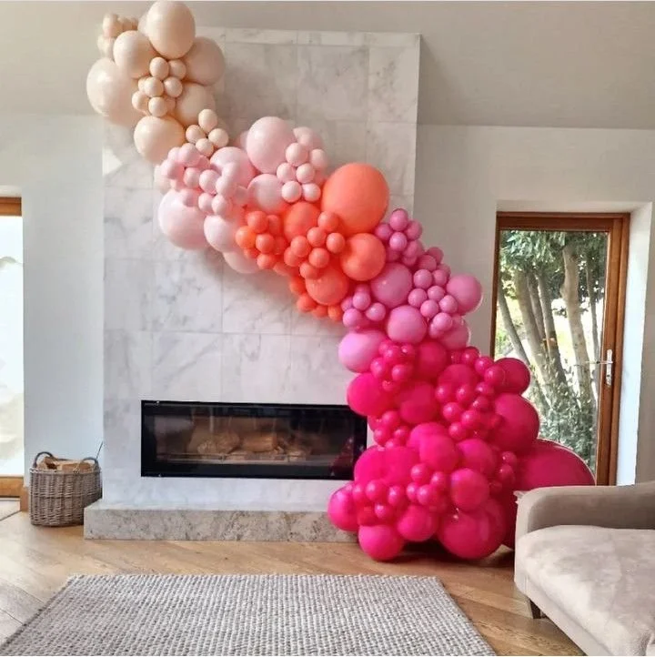 Organic balloon garland in Omaha hanging from ceiling to floor in front of fireplace featuring pink, coral, and white balloons for elegant event decoration and backdrop installation.