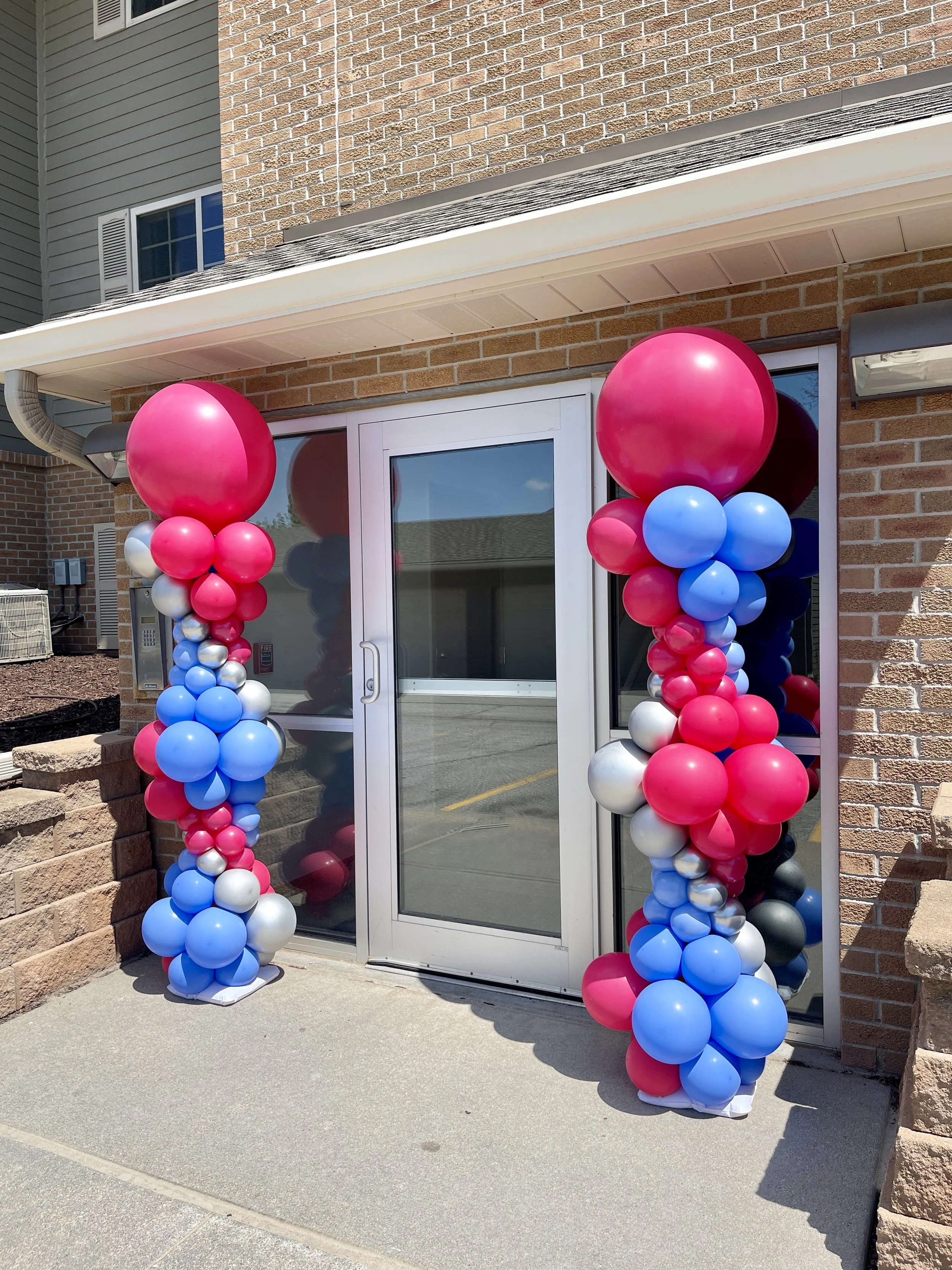 Grand opening balloon columns in Omaha featuring bright pink, blue, and silver balloons for storefront event decoration and business opening celebration.