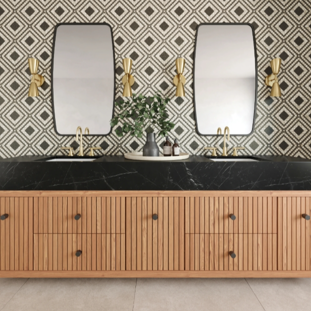 Double bathroom vanity with two rectangular mirrors, gold wall sconces, a black and gold countertop, a grey vase with green foliage, and small toiletries, against a geometric patterned tile wall.
