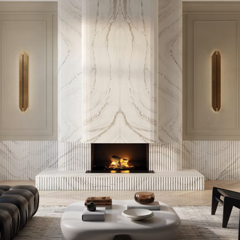 Modern living room with a white marble fireplace and built-in wall panels with gold accents, a black leather sofa, and a round coffee table with decorative items.