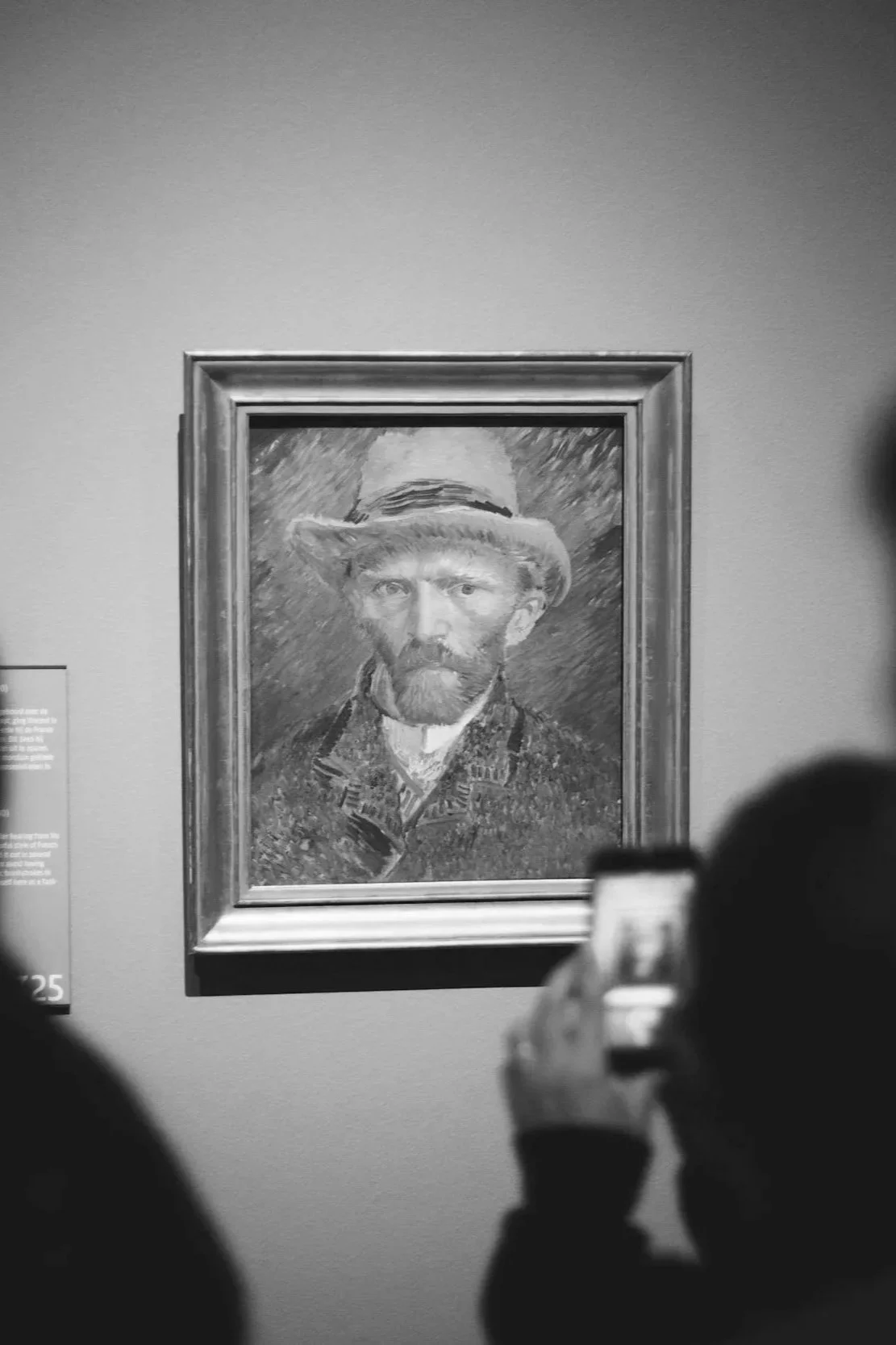 Meity Curator API - black and white photograph of a portrait of a man with a beard and a hat, displayed in a frame on a gallery wall. Visitors are taking pictures of the portrait.